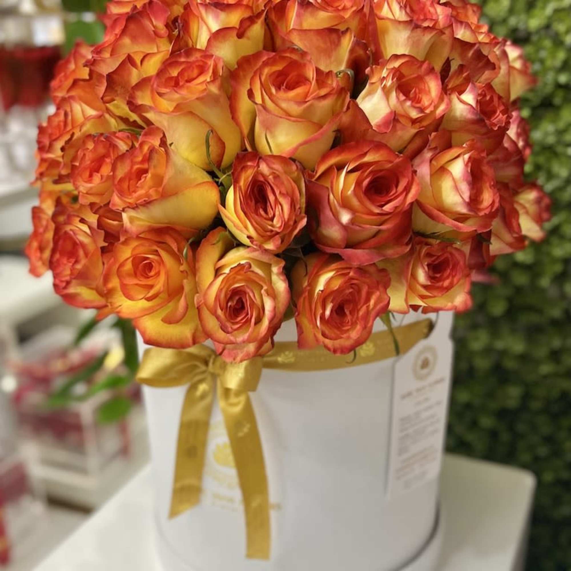 Round box of orange and yellow roses arranged tightly with a gold ribbon bow