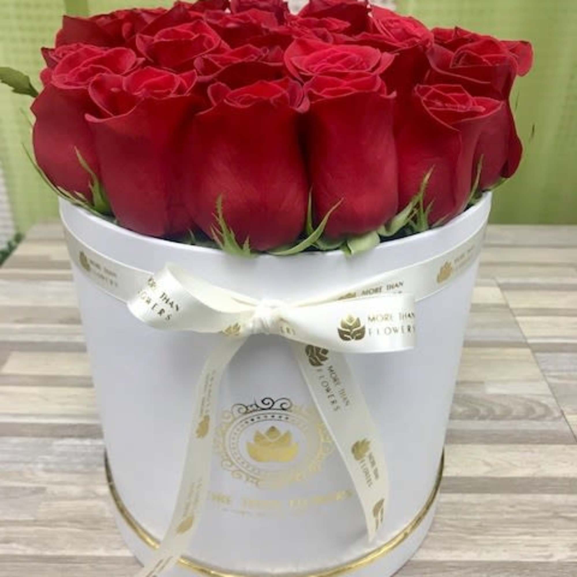 Round white hatbox filled with tightly packed red roses and tied with a cream ribbon bow.