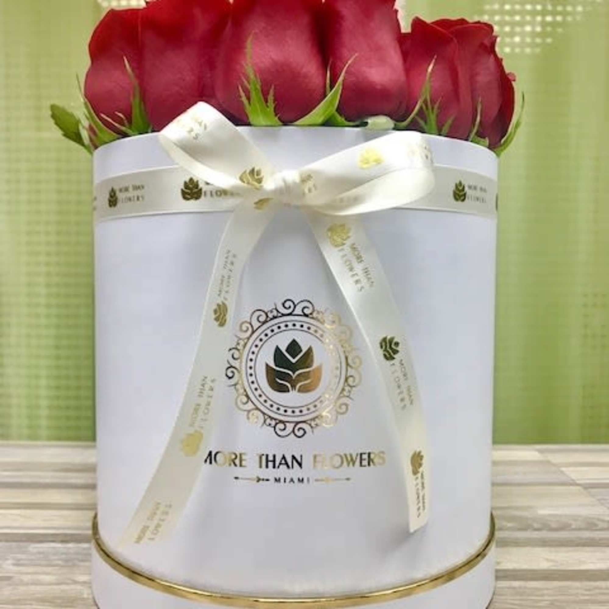 Red rose heads arranged in a white round hat box with a cream ribbon bow.