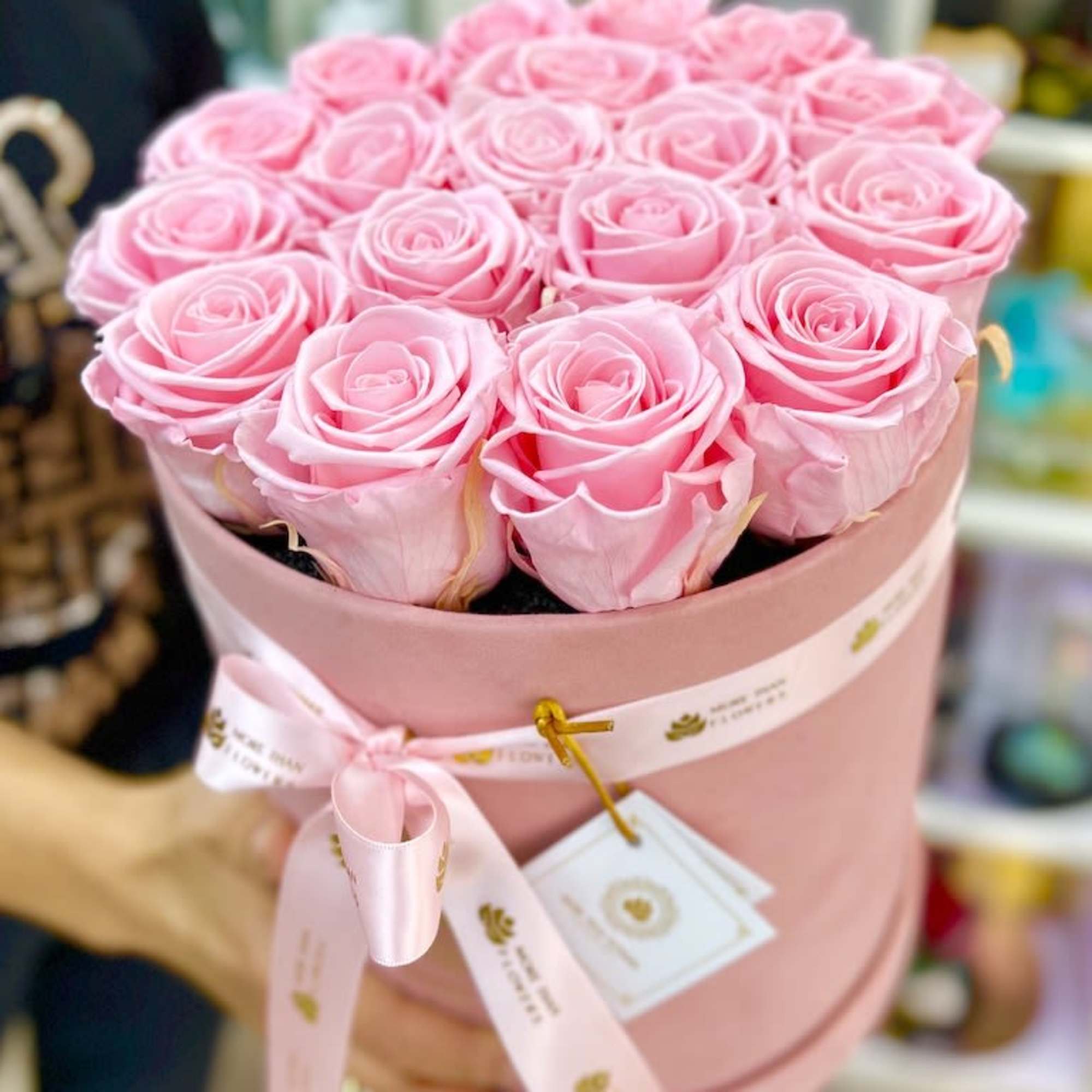 Pink hat box filled with tightly packed light pink roses and tied with a matching ribbon