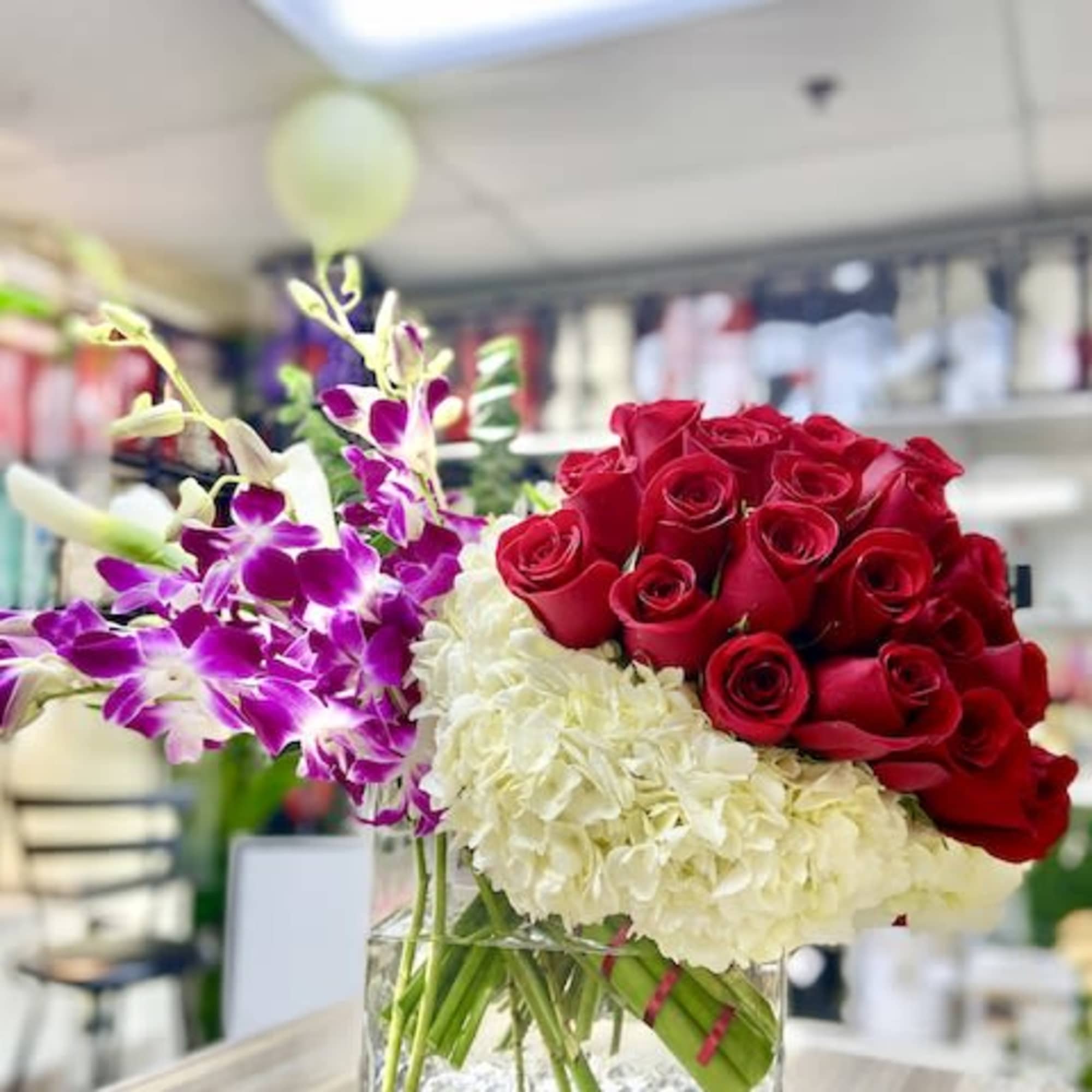 Low modern arrangement of red roses, white hydrangeas, and purple orchids in a clear glass cube vase