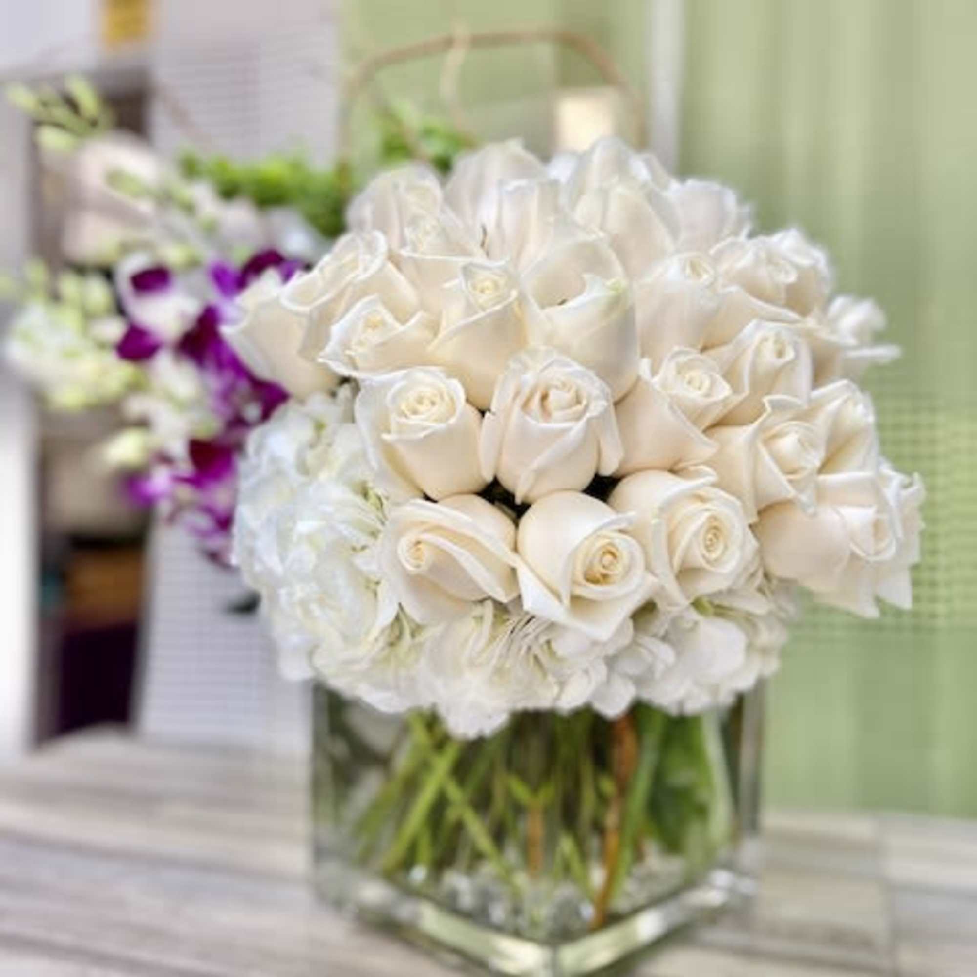 Compact arrangement of white roses in a clear square glass vase on a wooden surface.