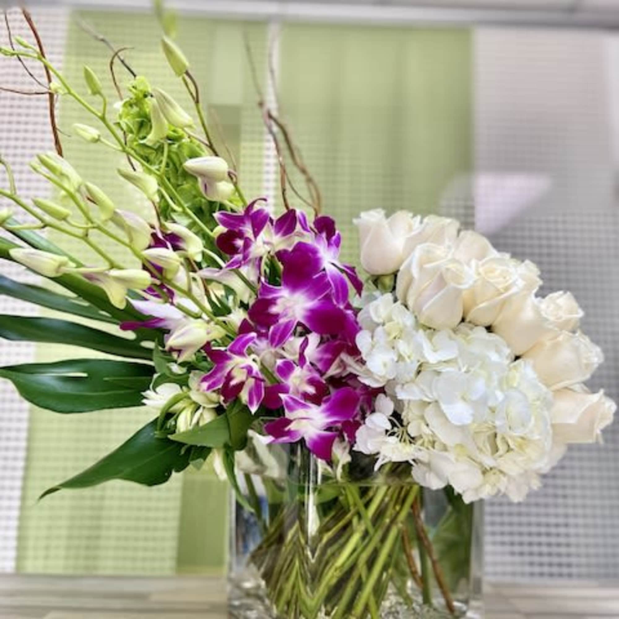 Asymmetrical arrangement of purple orchids, white roses, and white hydrangeas in a clear glass cube vase.