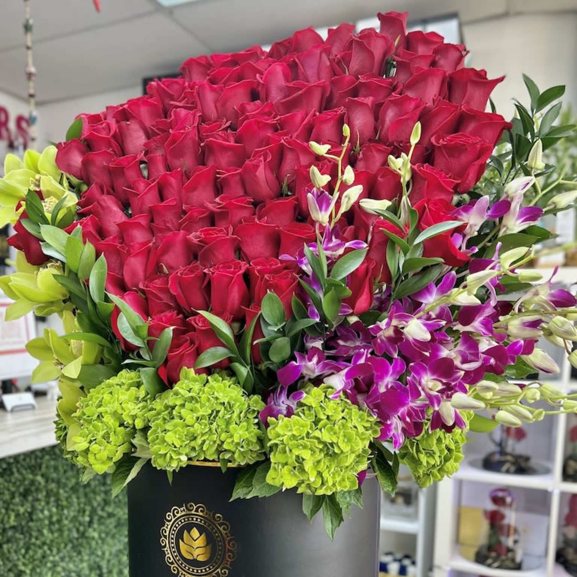 Large hatbox arrangement of red roses with green hydrangeas and purple orchids in a black round box