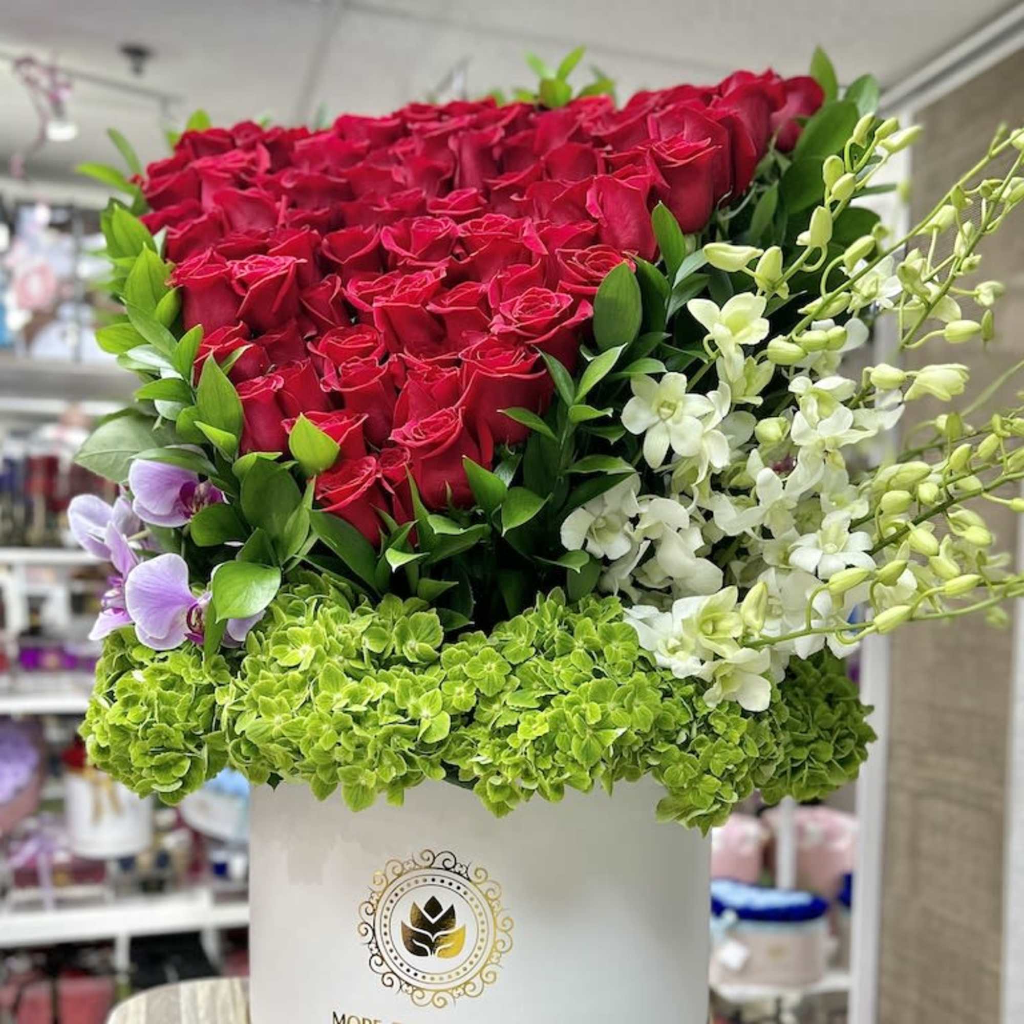 Tall hatbox arrangement of red roses, green hydrangeas, and white and purple orchids in a white box