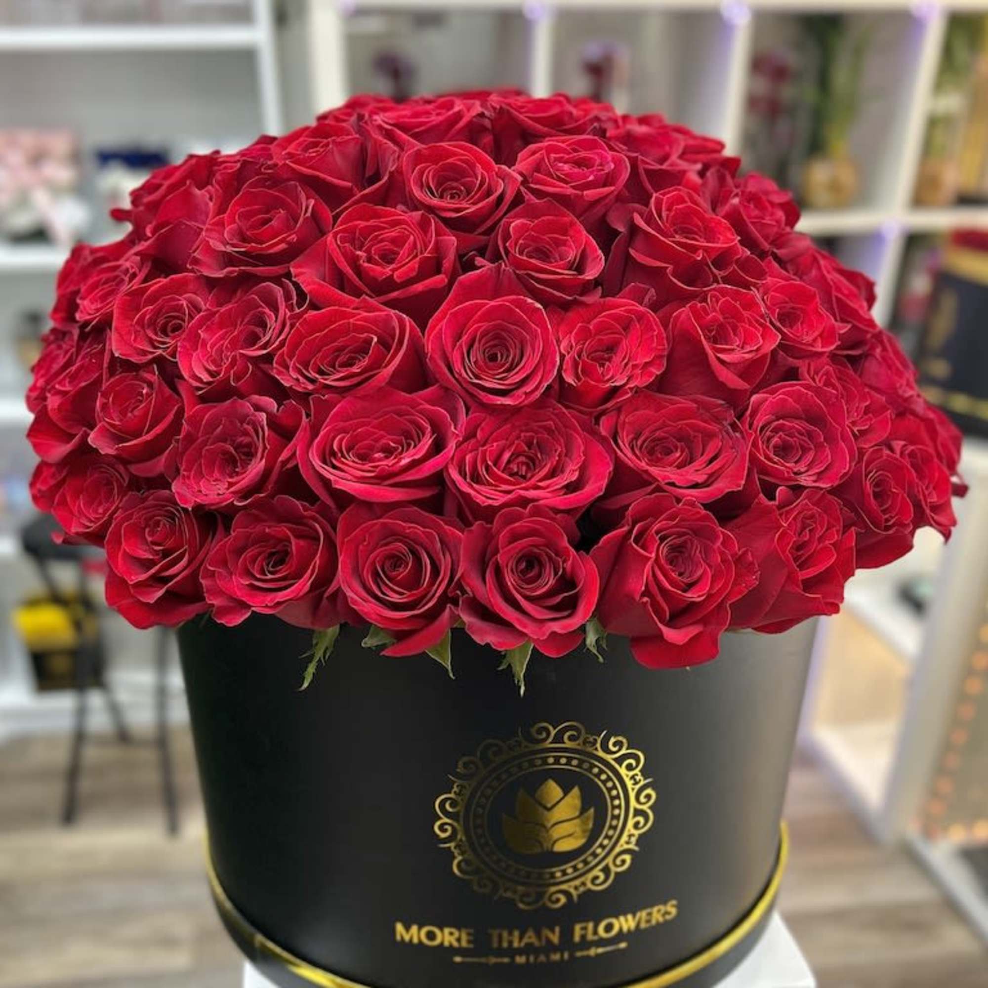 Large round box of tightly packed red roses in a black hatbox-style container