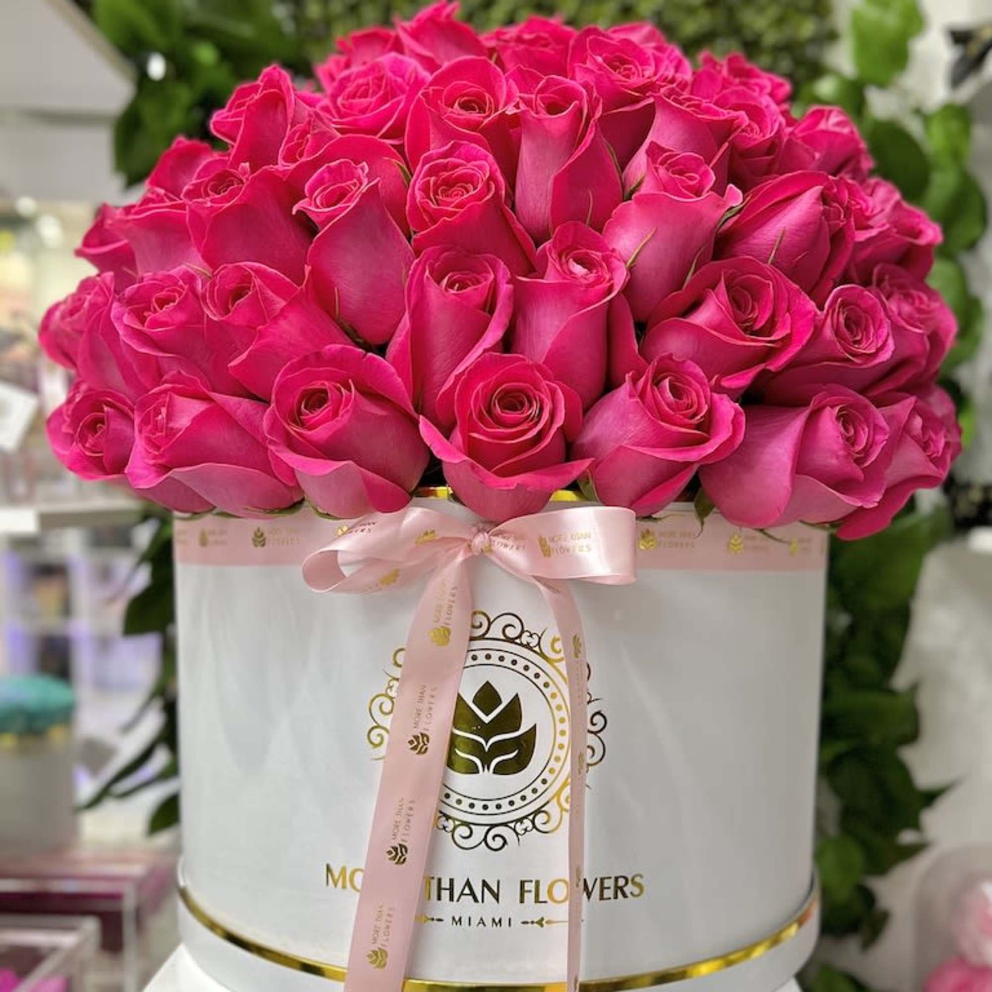 Round white box filled with bright pink roses and tied with a pink ribbon