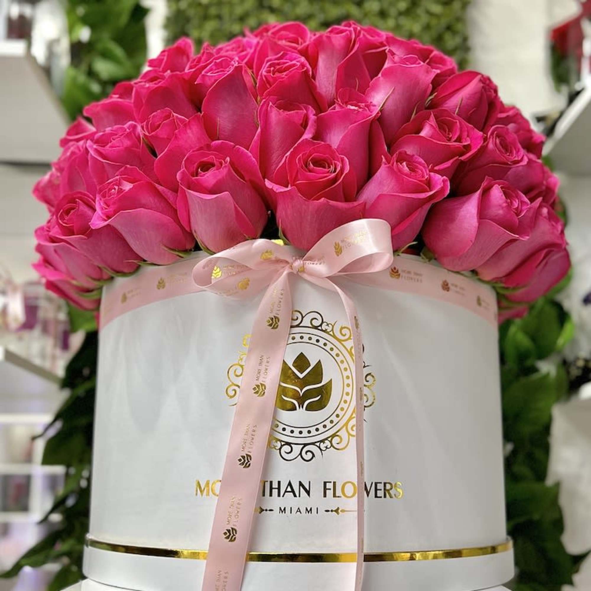 Round white box filled with tightly packed hot pink roses and tied with a pink ribbon.