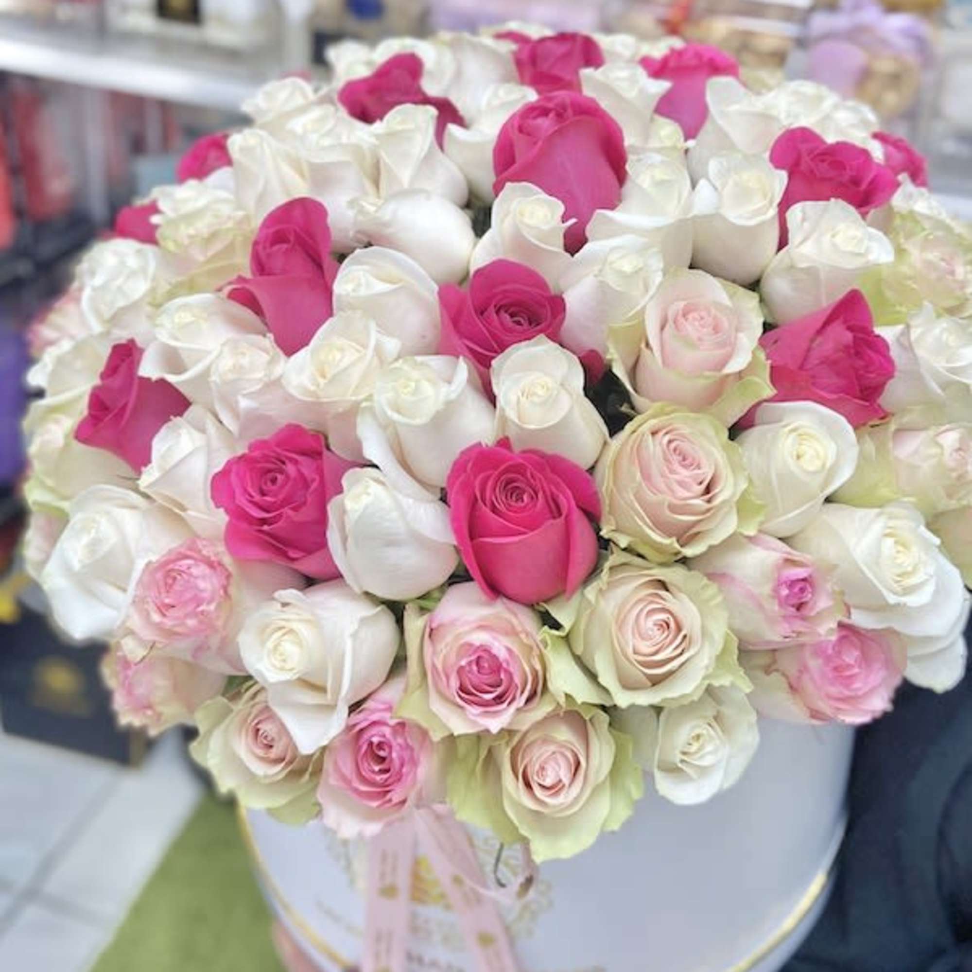 Round hatbox filled with white, cream, and bright pink roses held in both hands