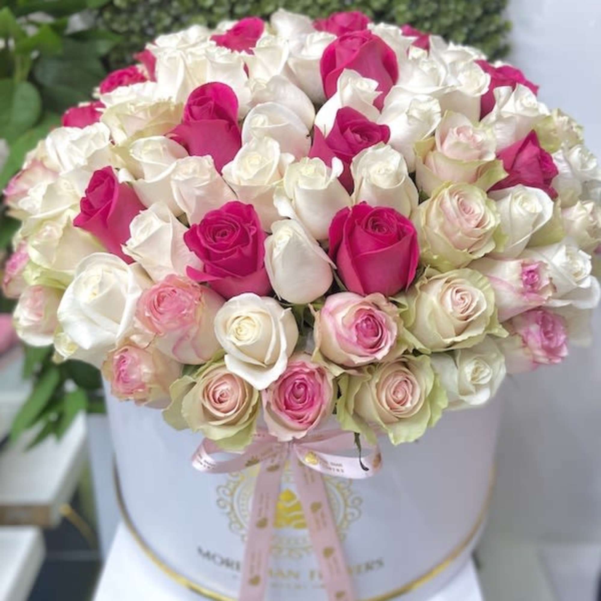 Round white hatbox filled with pink and white roses, tied with a pale pink ribbon.