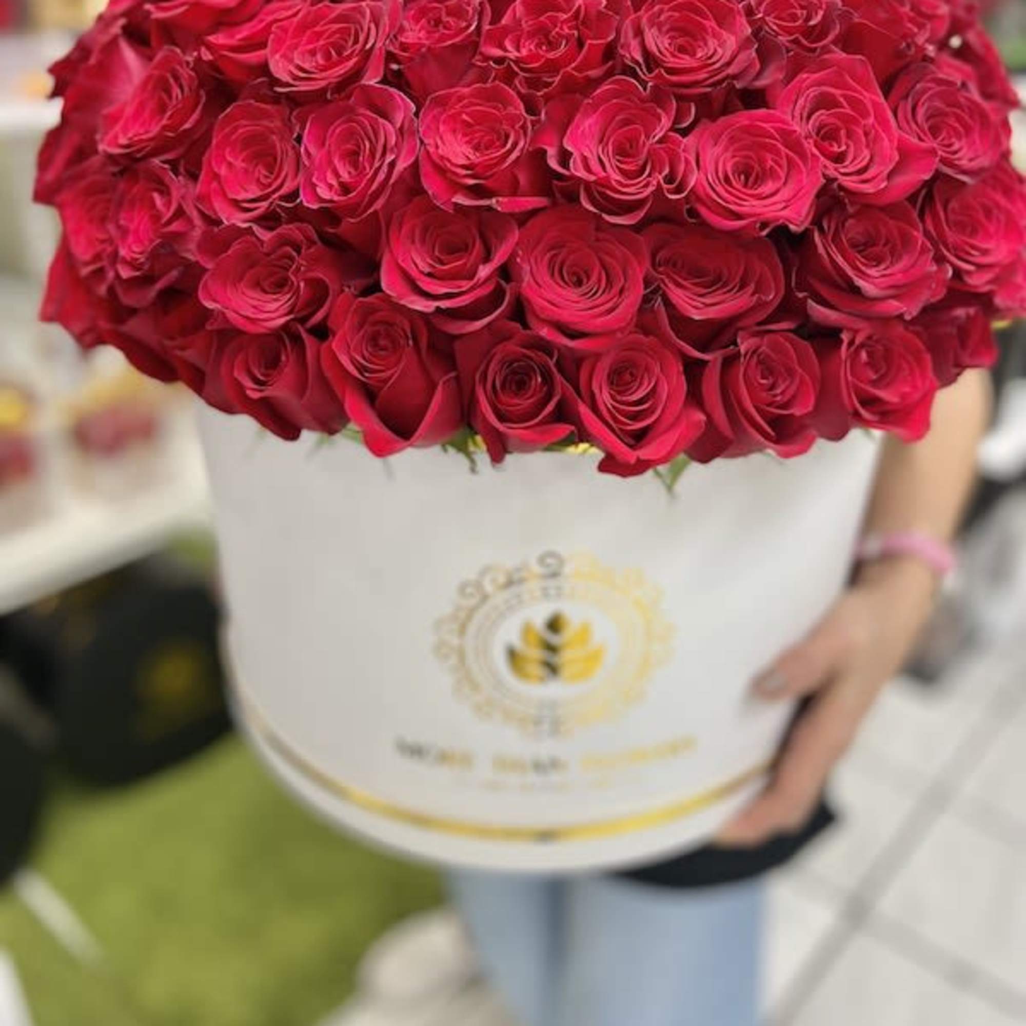 Large round box of tightly packed red roses held by a person