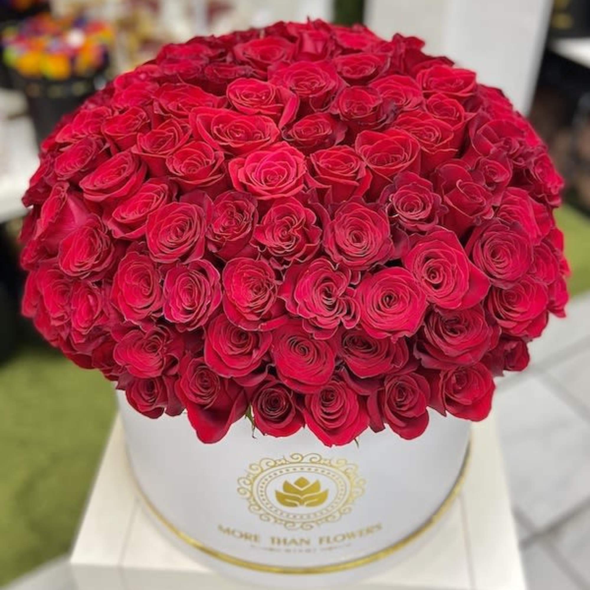 Large round box filled with tightly packed bright red roses on a white stand
