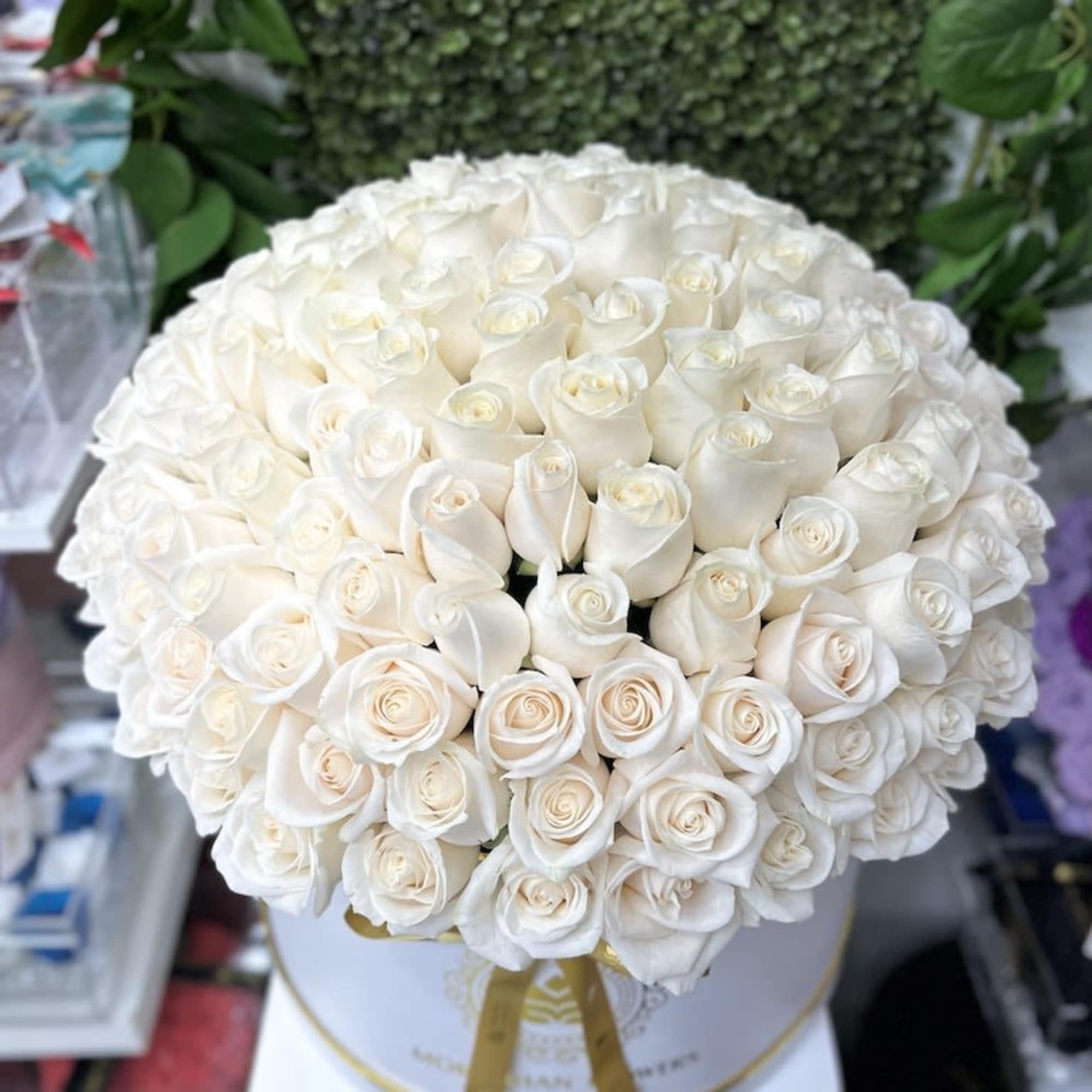 Large round box filled with tightly packed white roses, finished with a gold ribbon