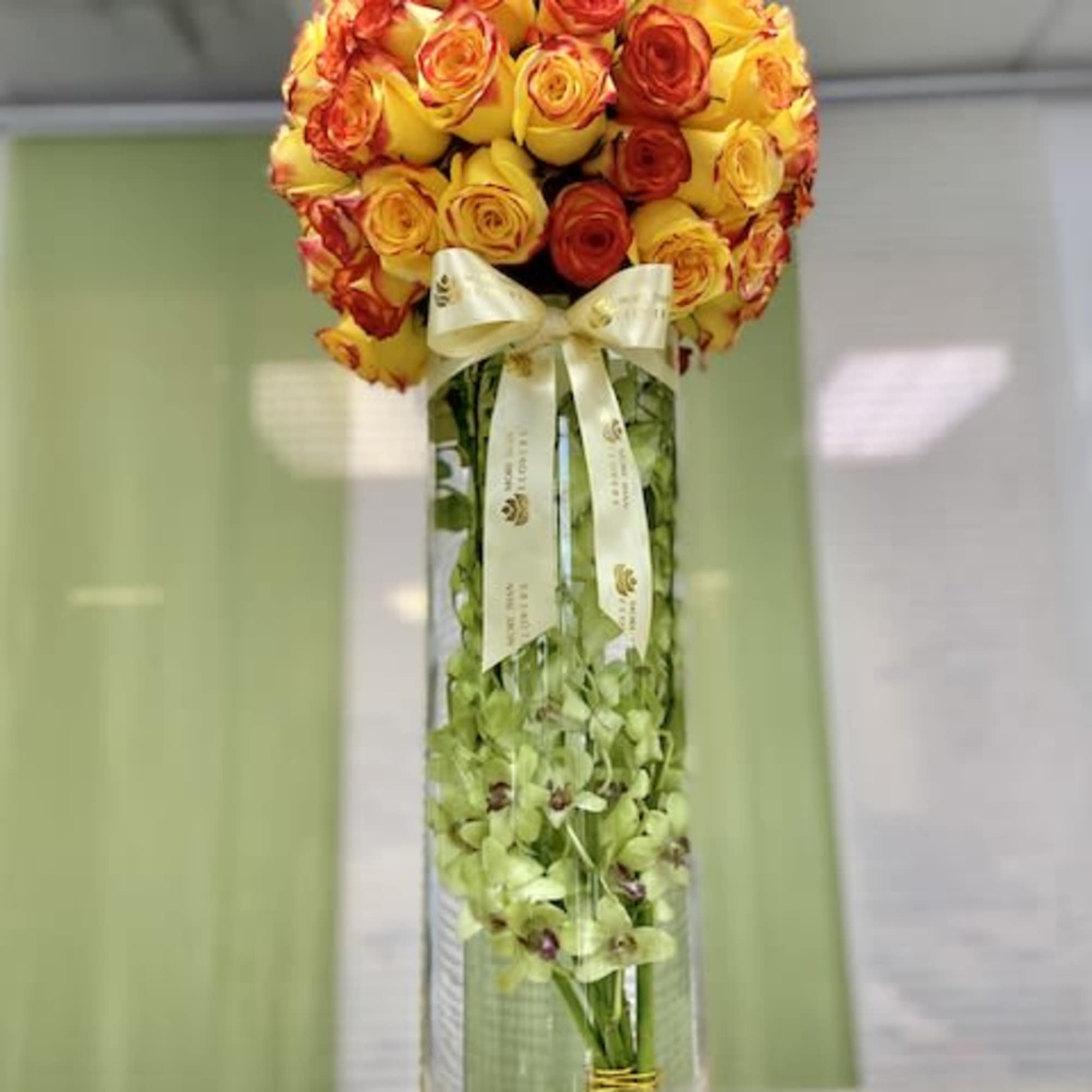Tall glass vase with submerged green orchids and a dome of yellow and orange roses on top