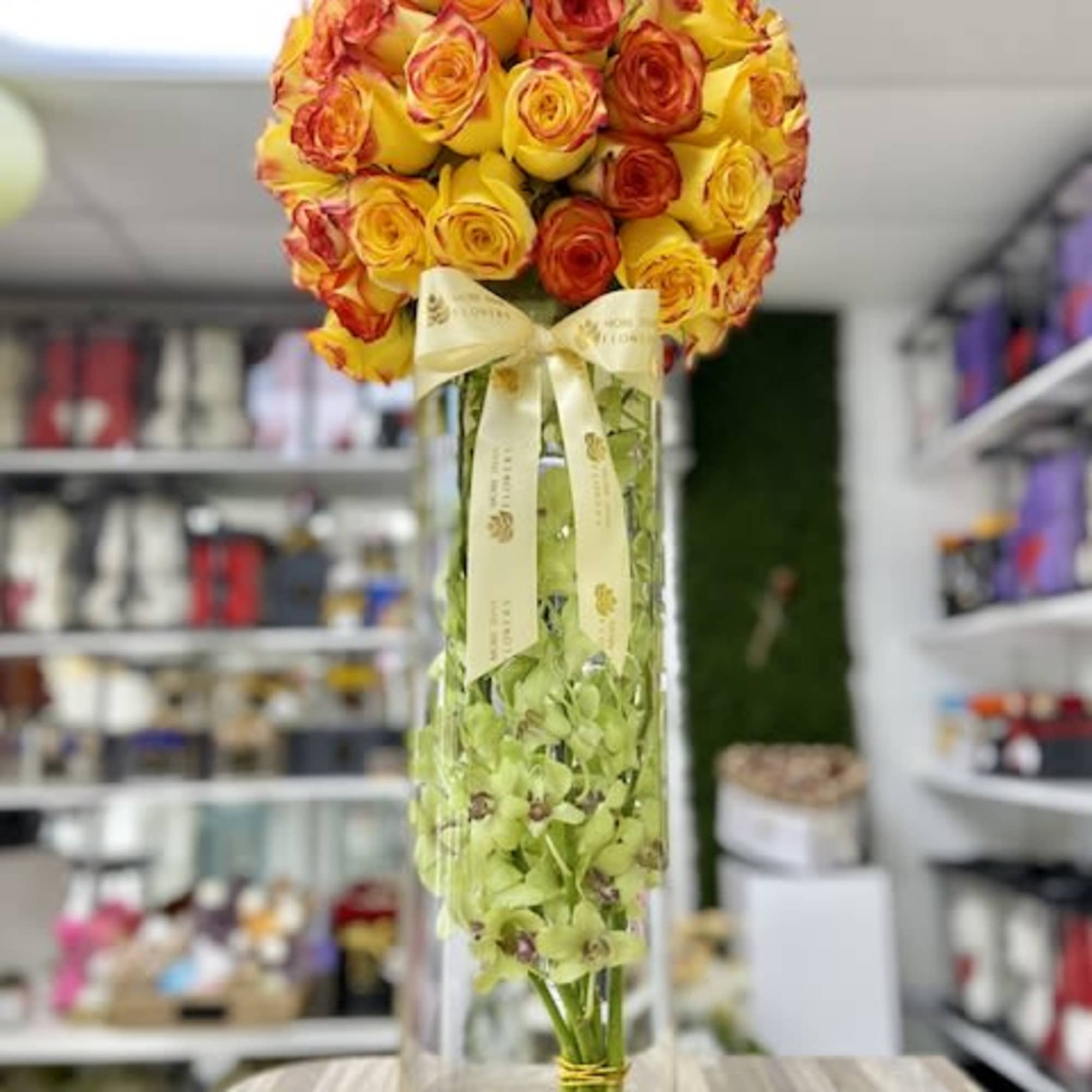 Tall glass vase with yellow and orange rose sphere and green orchids inside the vase