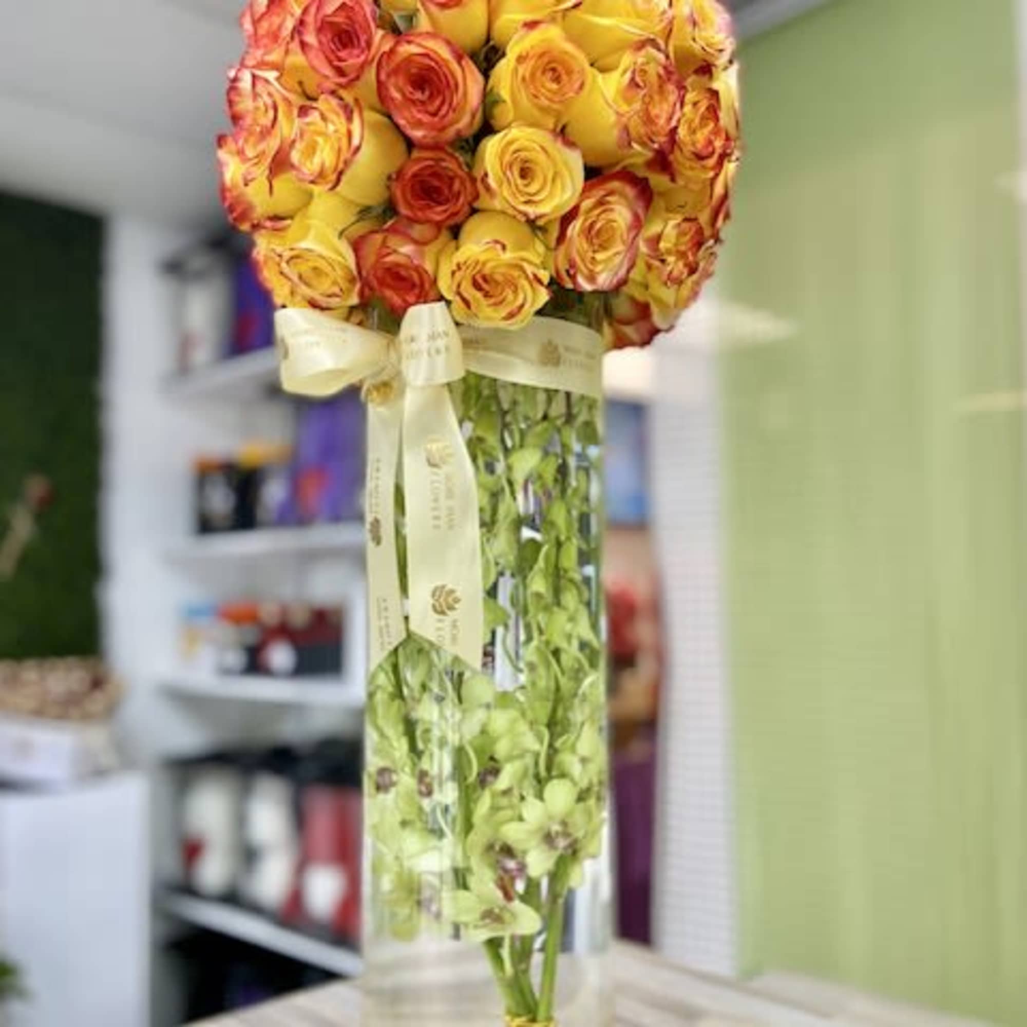 Tall cylinder vase with yellow and orange roses on top and green orchids submerged inside.