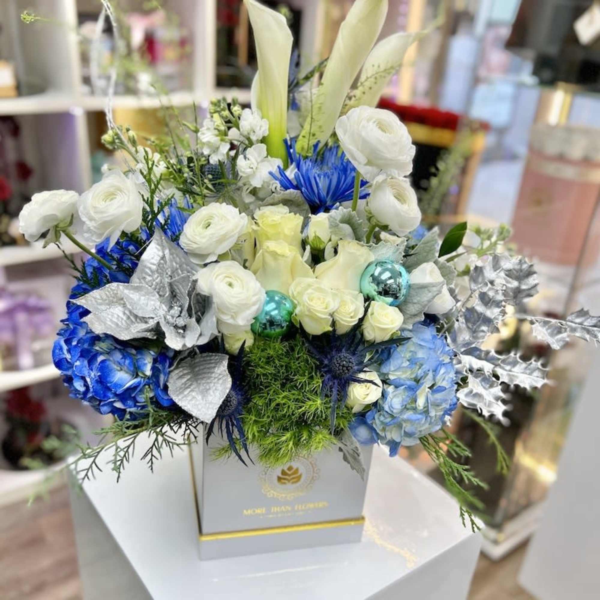 Box arrangement of white calla lilies, roses, and blue hydrangeas with silver accents in a white square container
