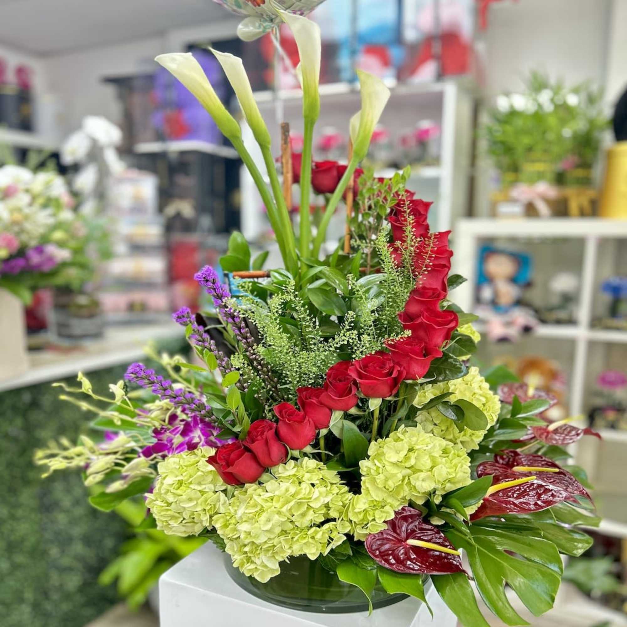 Tall mixed arrangement with white calla lilies, red roses, green hydrangeas, and red anthuriums in a glass vase