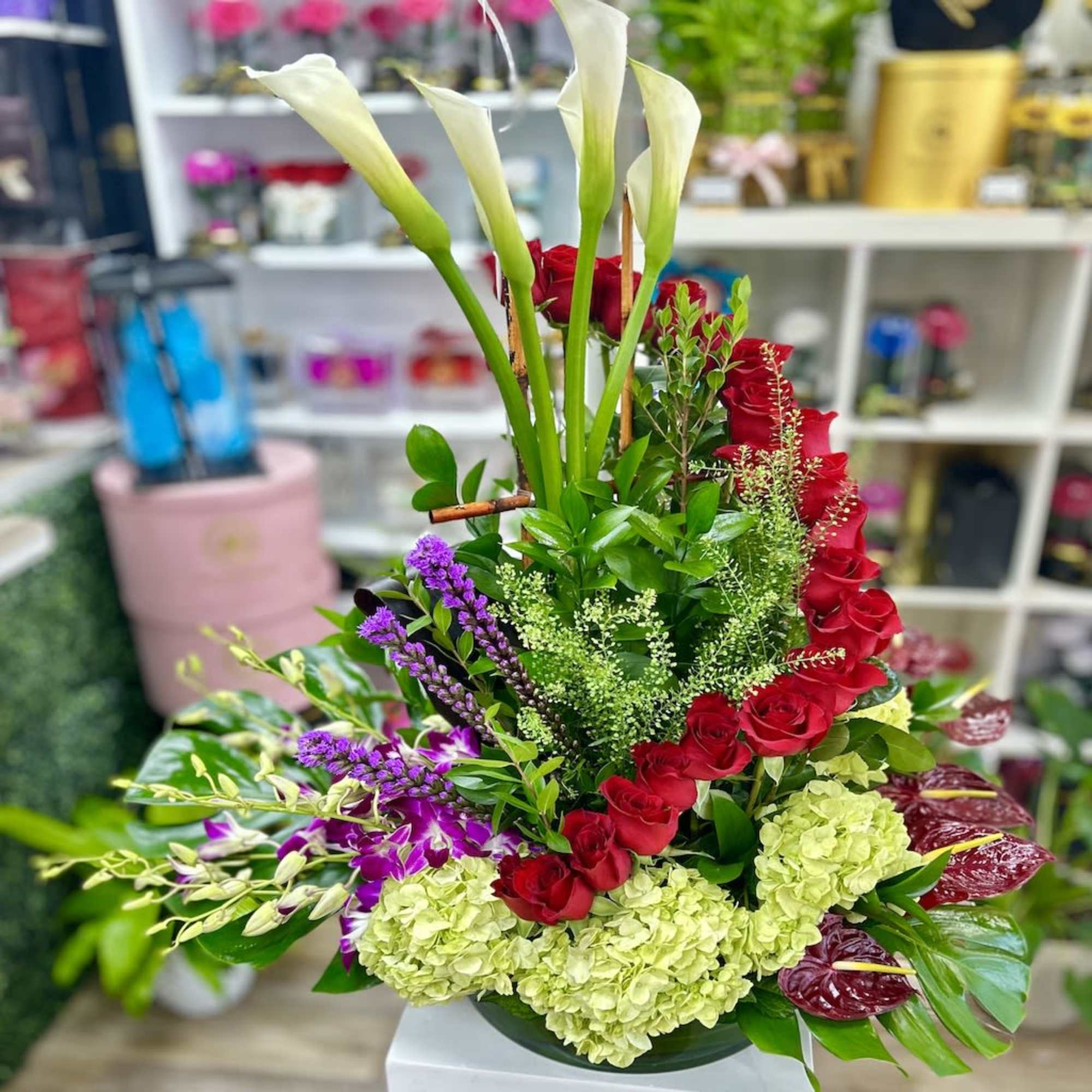 Tall mixed arrangement with white calla lilies, red roses, green hydrangeas and orchids in a low round bowl