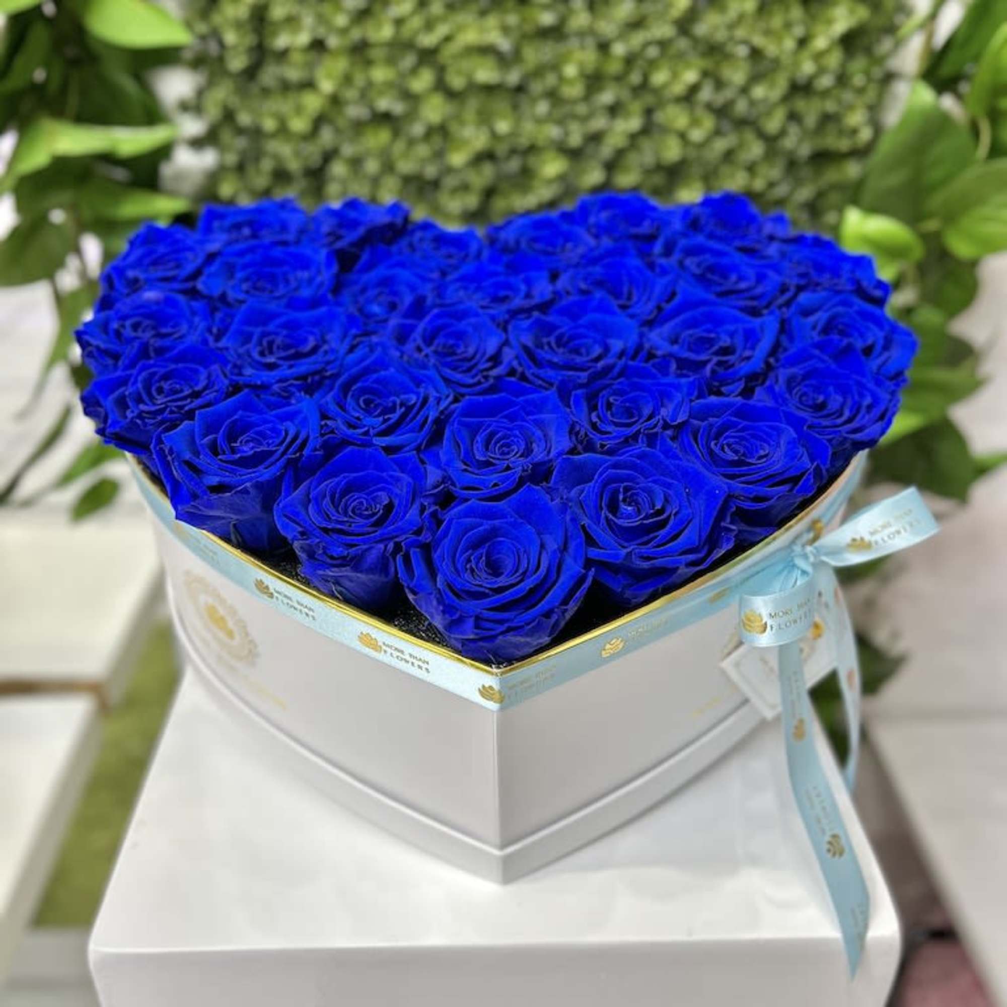 Heart-shaped box filled with vivid blue roses and tied with a light blue ribbon