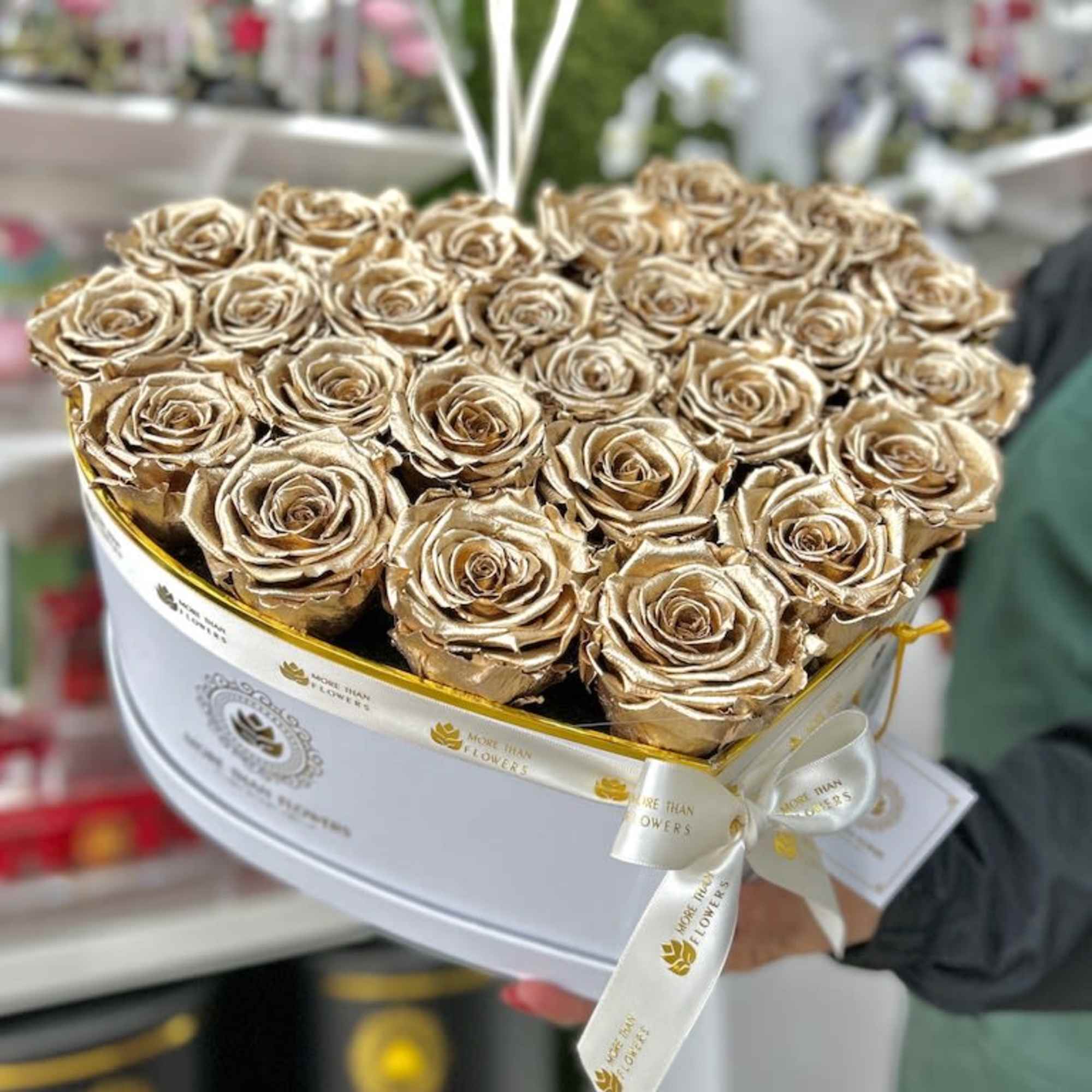 Heart-shaped white box filled with metallic gold roses and tied with a white logo ribbon