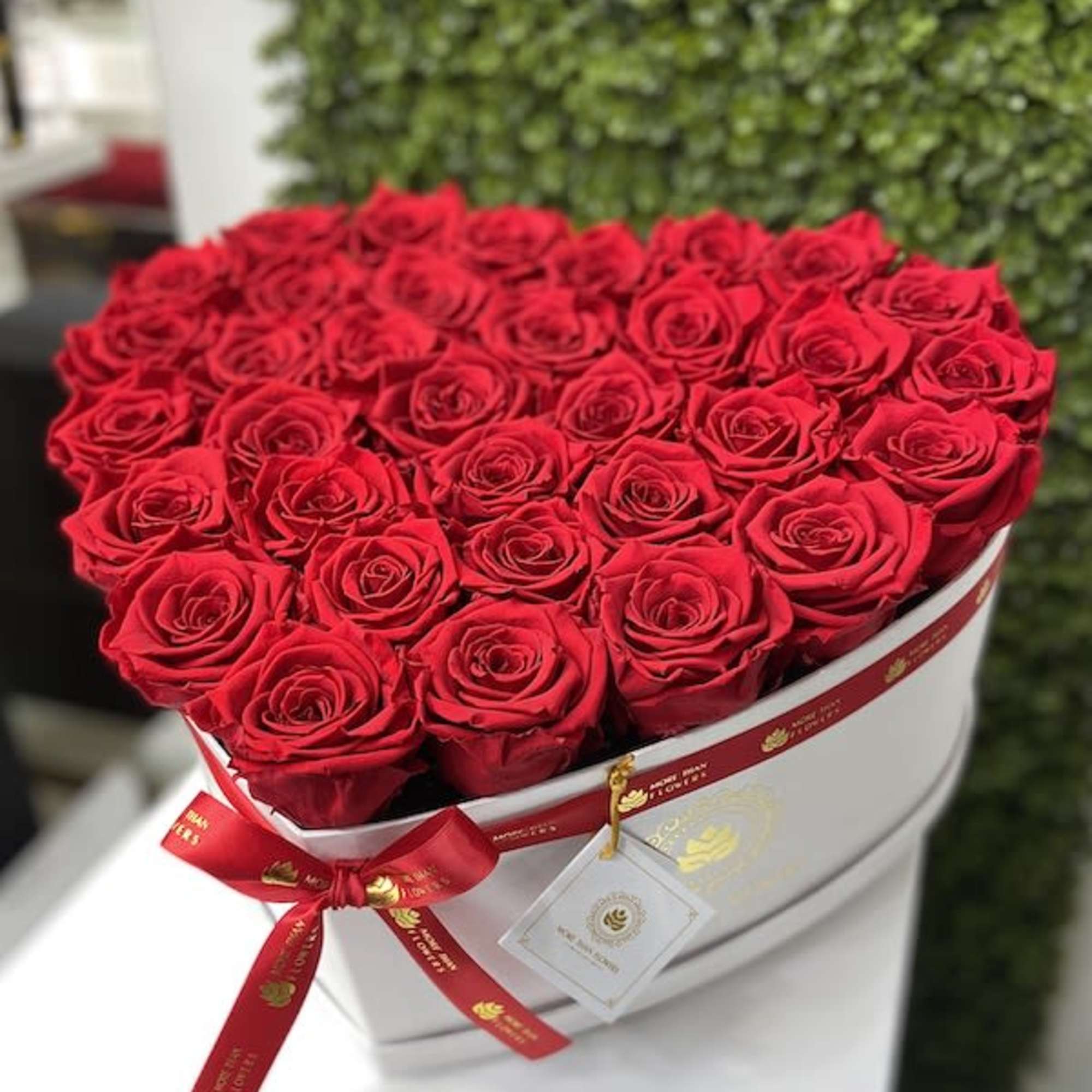 Heart-shaped white box filled with tightly packed red roses and a red ribbon bow.