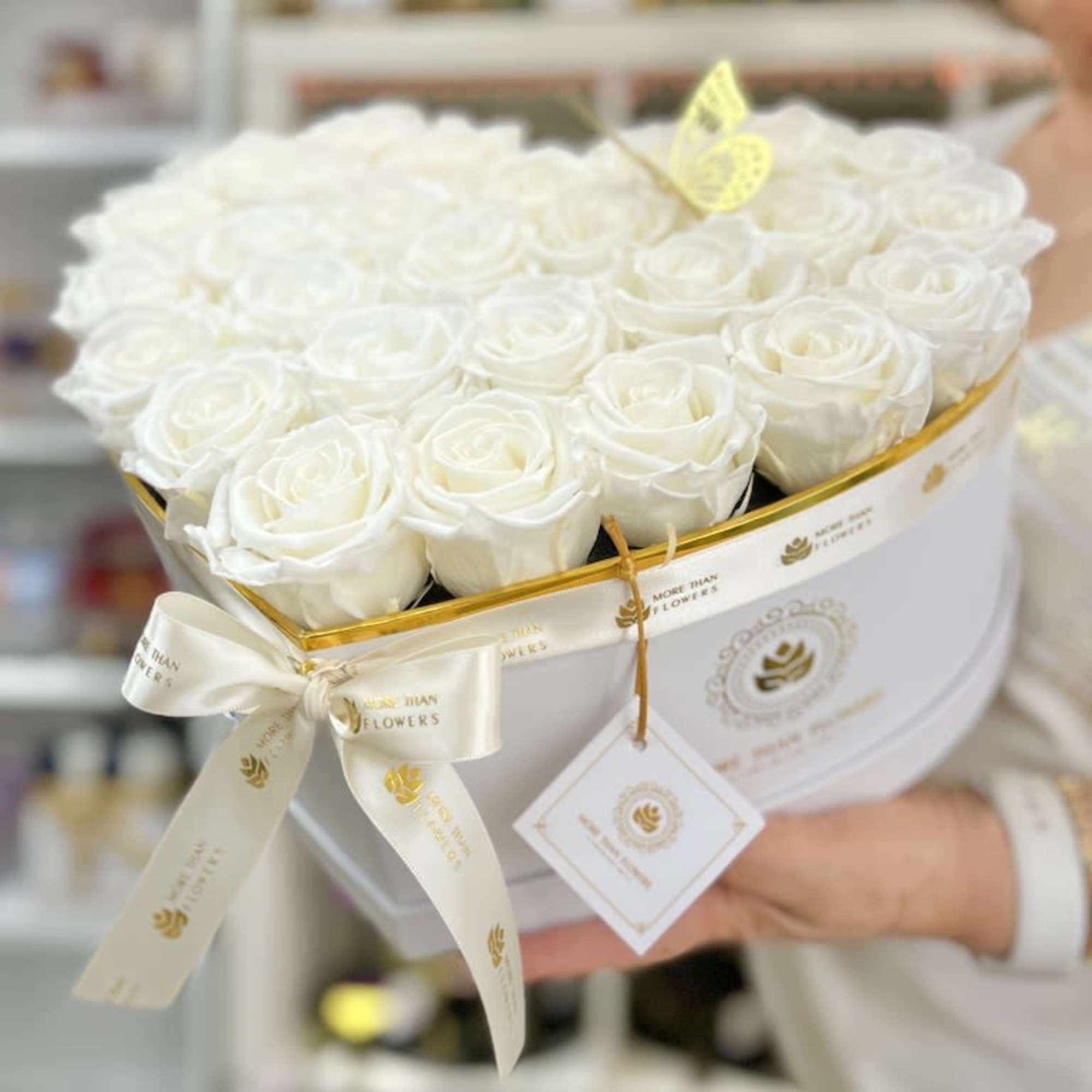 Heart-shaped white box filled with white roses, tied with a white ribbon and tag.
