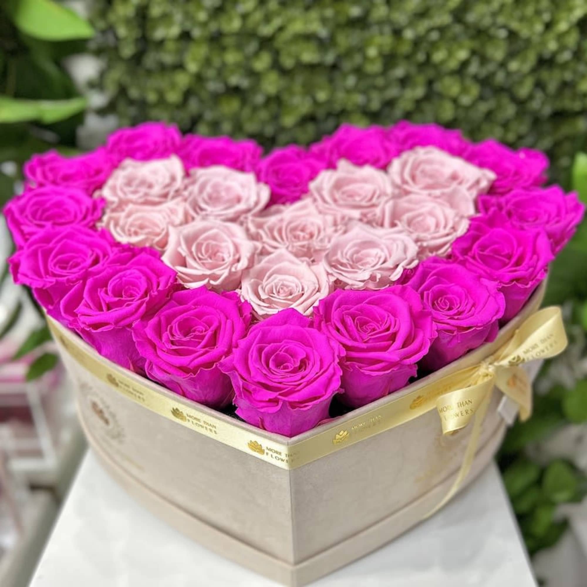 Heart-shaped box filled with hot pink and light pink roses tied with a cream ribbon.