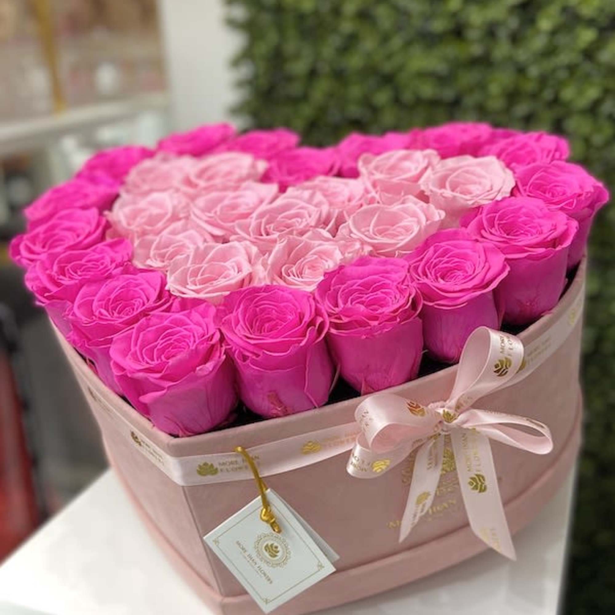 Heart-shaped box of bright and light pink roses with ribbon and tag
