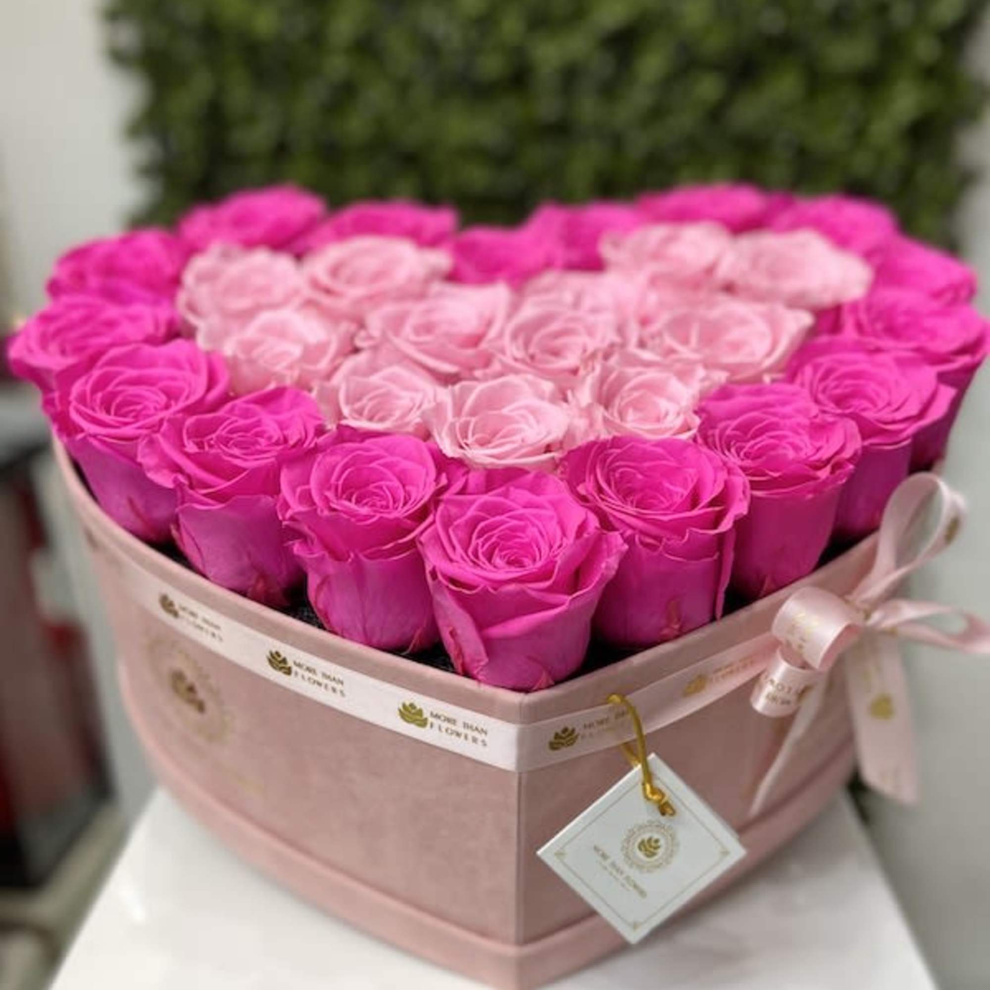 Heart-shaped pink box filled with hot pink and light pink roses with ribbon and tag