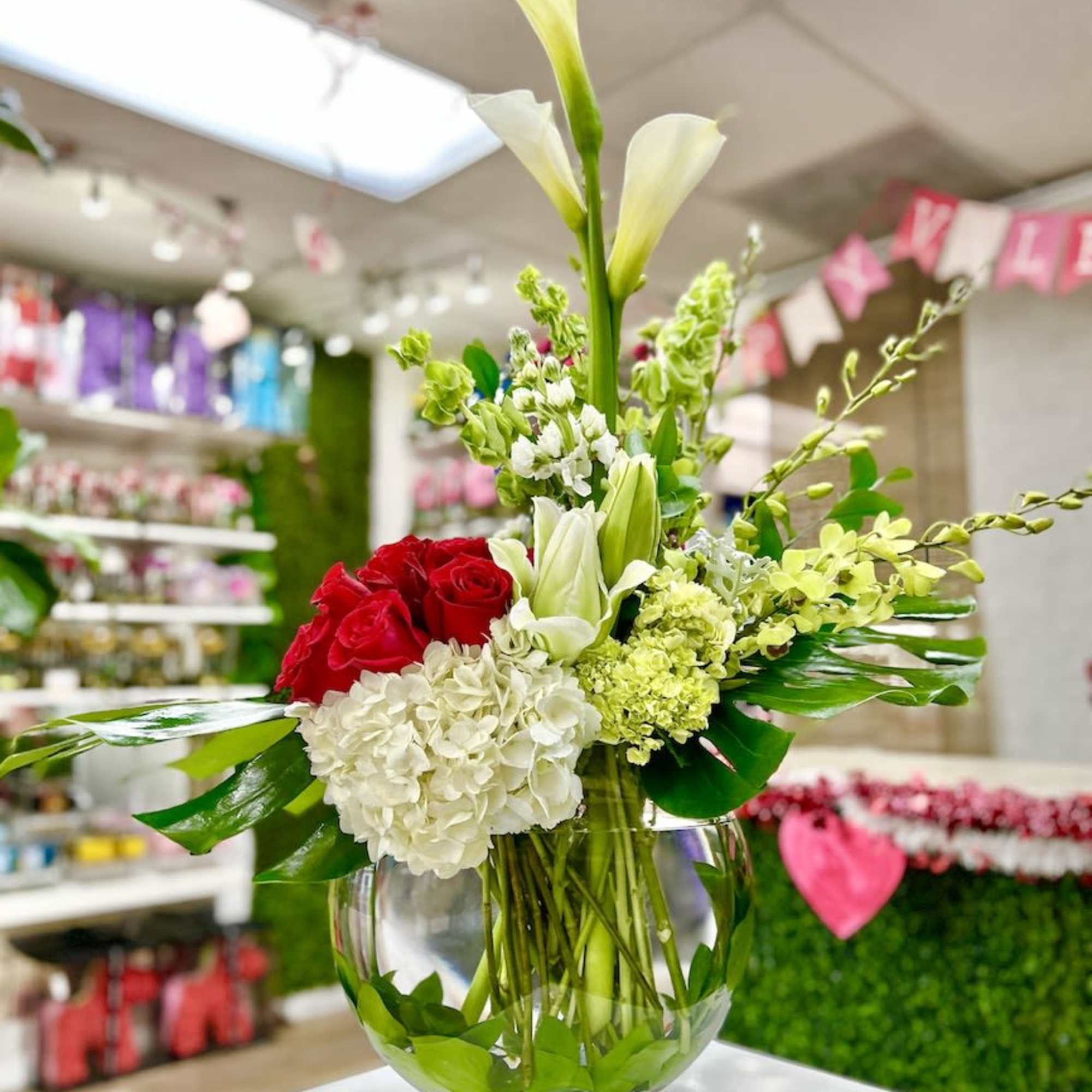 Low glass bowl of red roses, white hydrangeas, calla lilies and green blooms in an asymmetrical arrangement
