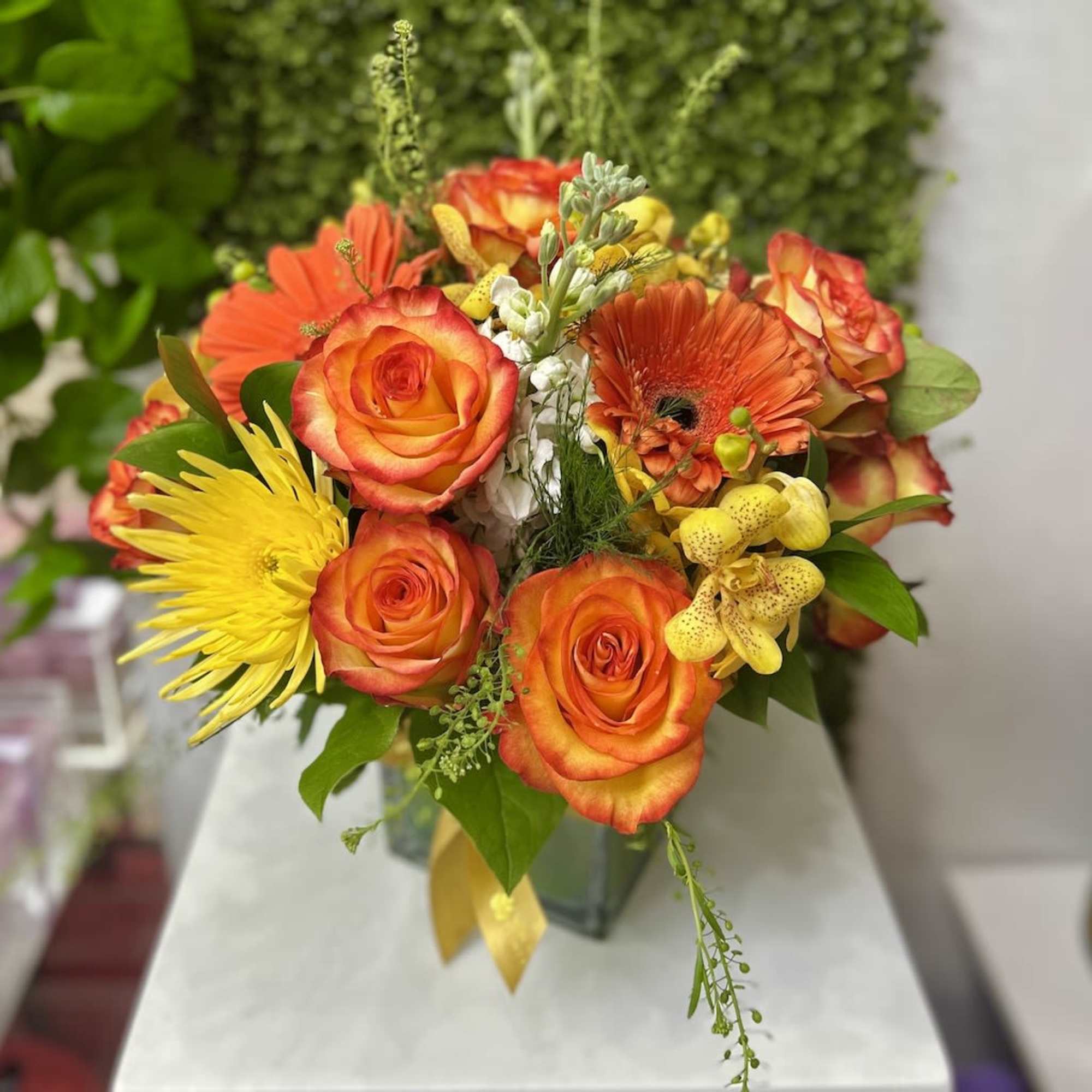 Bright arrangement of orange roses, yellow blooms, and orange gerbera daisies in a clear glass vase