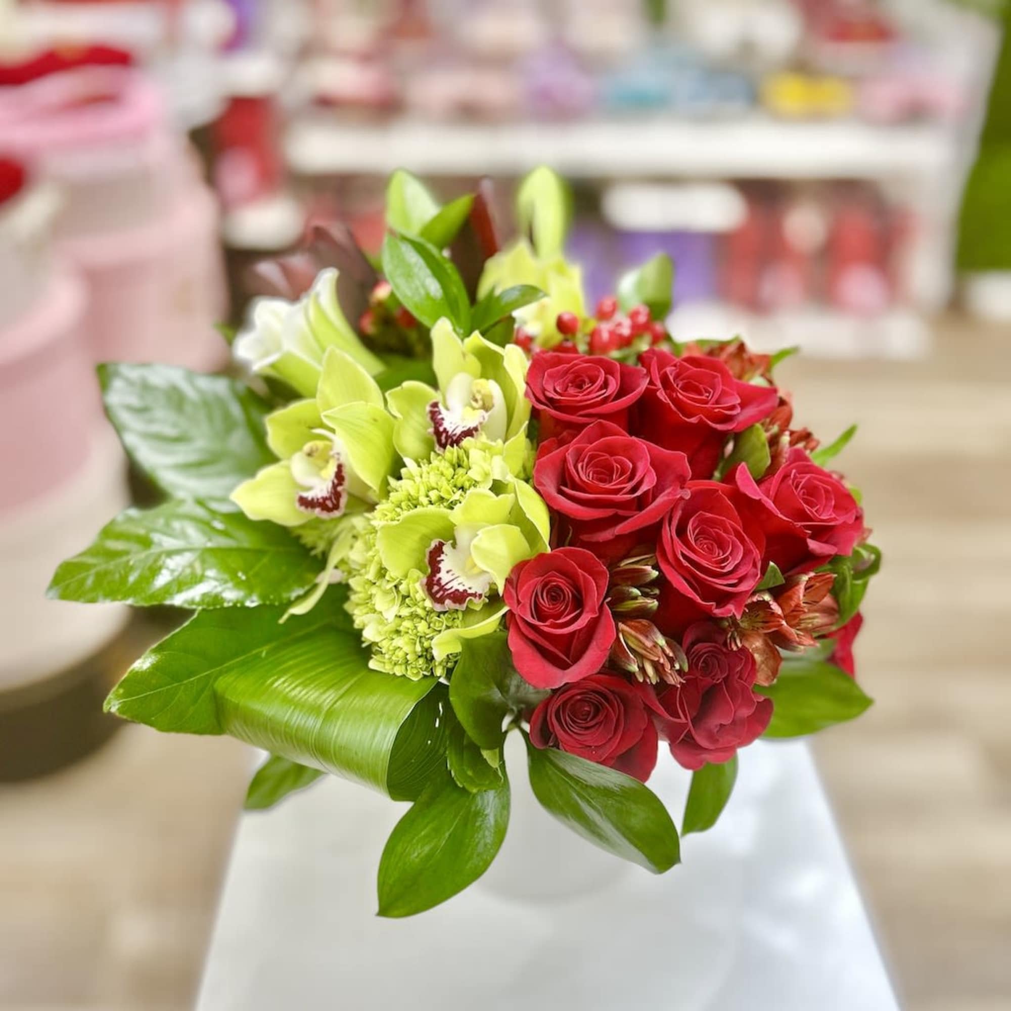Compact arrangement of red roses and green orchids in a white pedestal vase