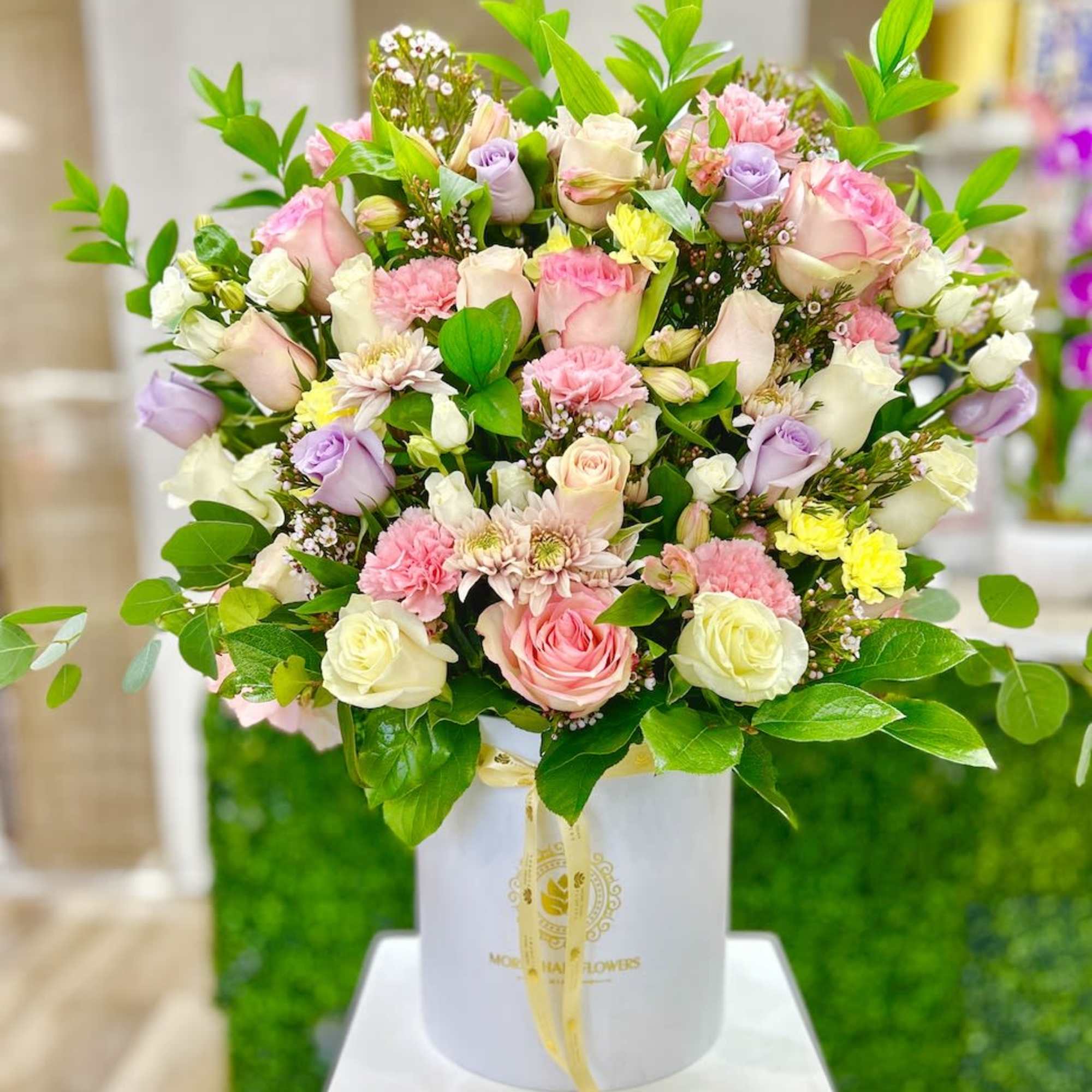 Pastel pink, white, and lavender flower arrangement in a white hatbox with ribbon