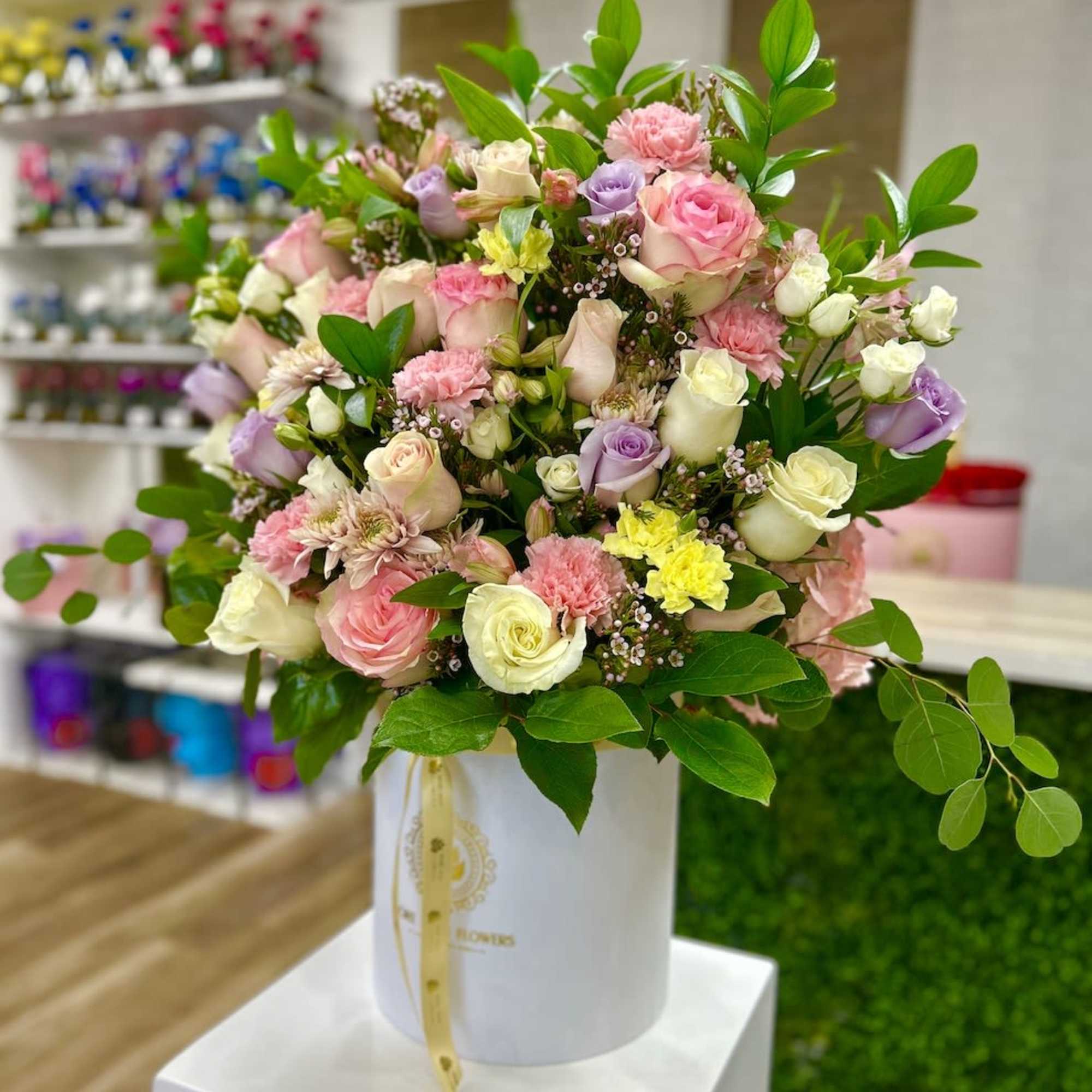 Pastel arrangement of roses, carnations, and mums in a white hatbox-style container