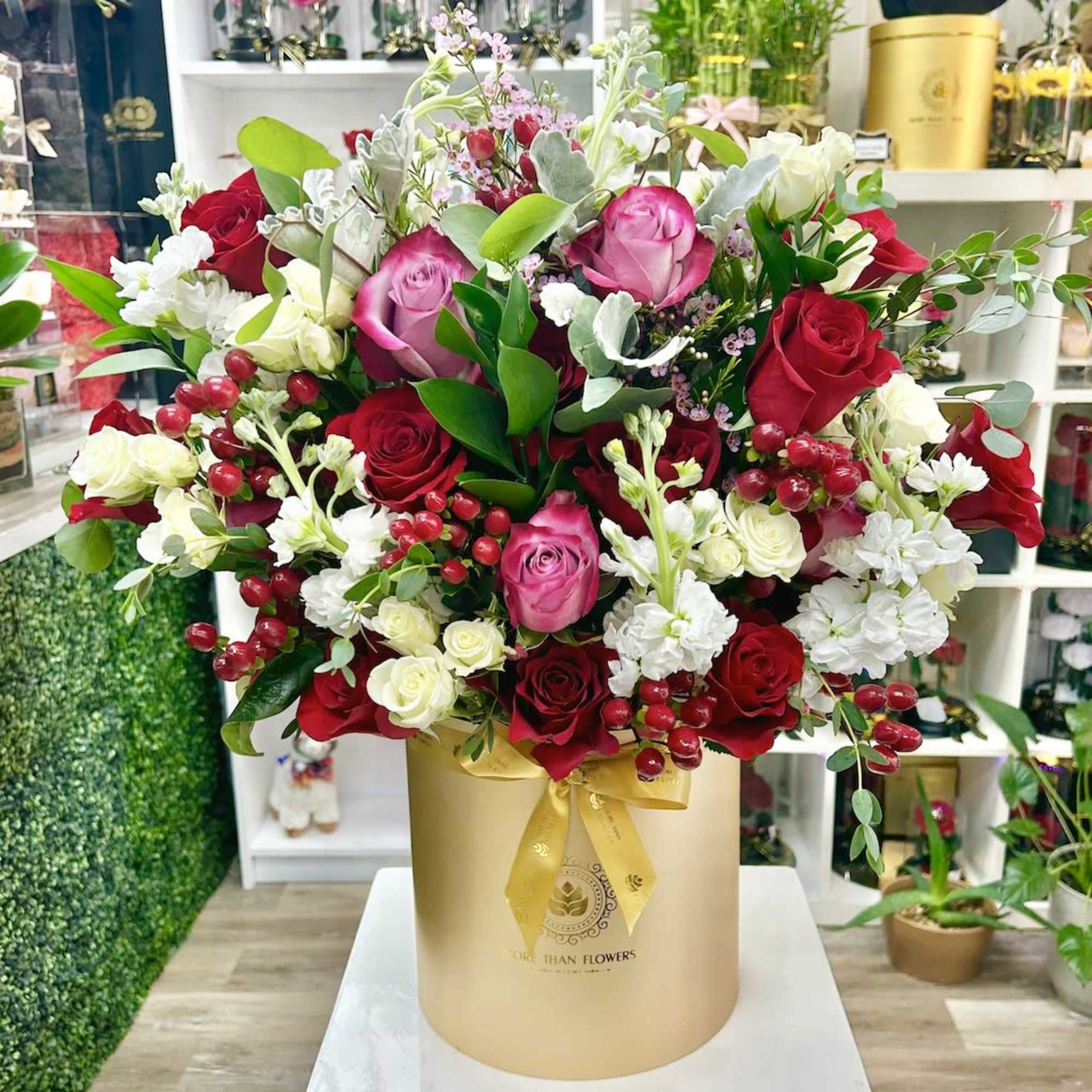 Large arrangement of red, pink, and white roses in a gold hatbox with ribbon