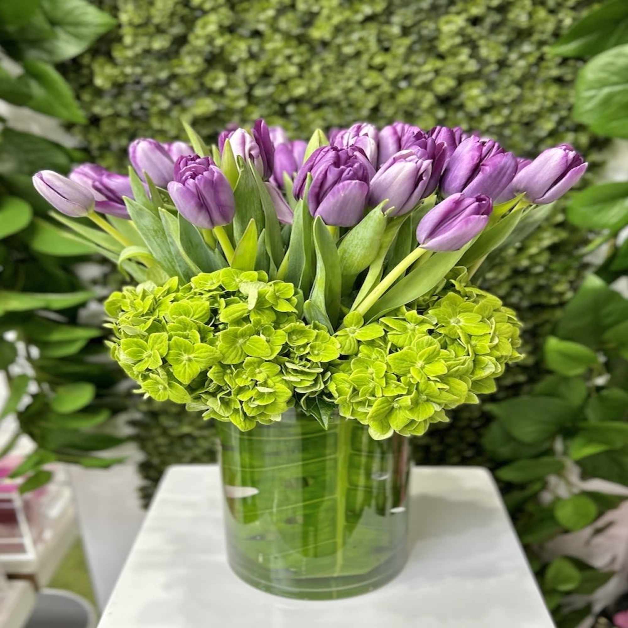 Tall glass vase with purple tulips and bright green hydrangeas in a compact, modern arrangement