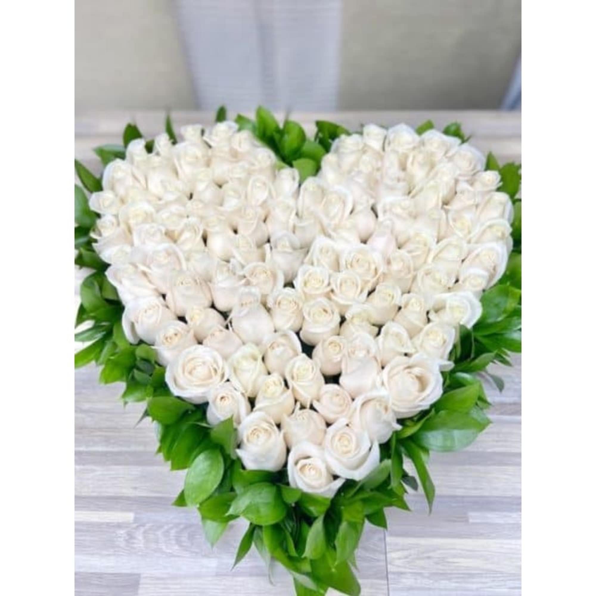 Heart-shaped arrangement of white roses edged with bright green foliage on a light wood surface