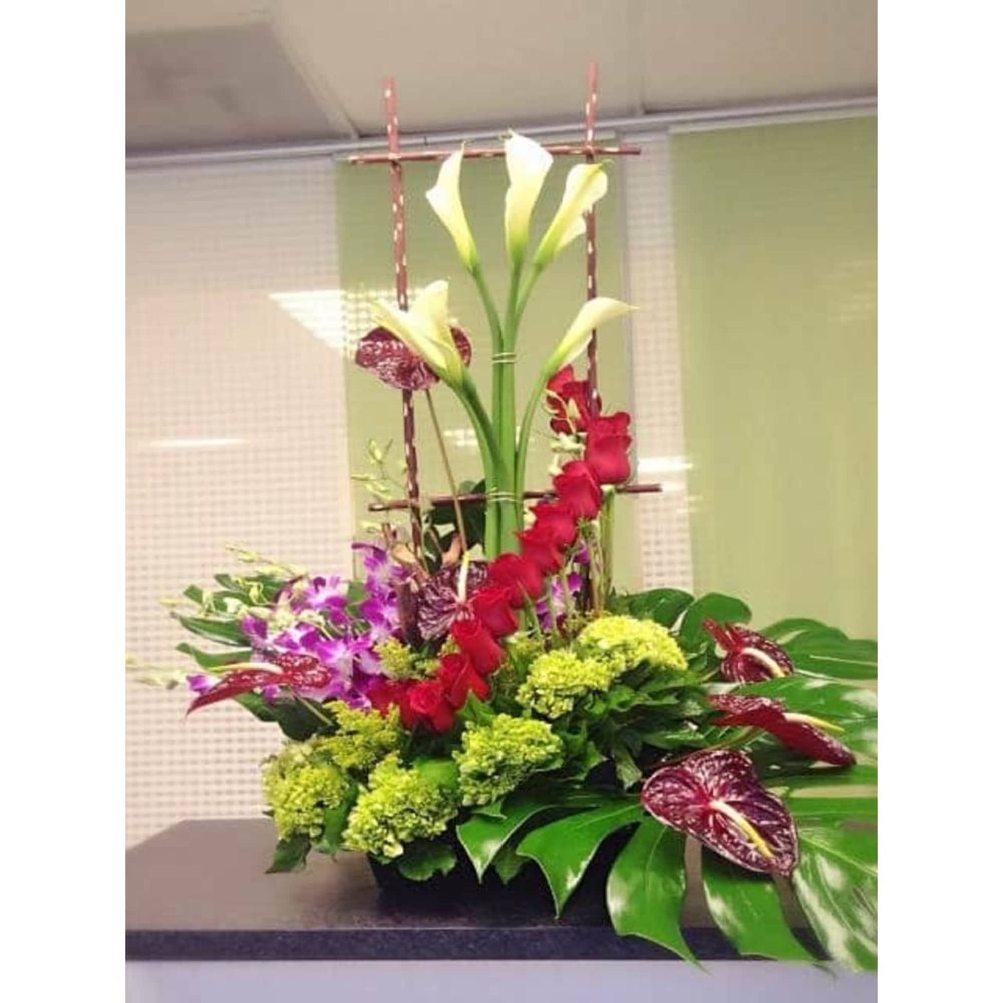 Tall modern arrangement with white calla lilies, red tropical blooms, orchids, and green hydrangea in a low container