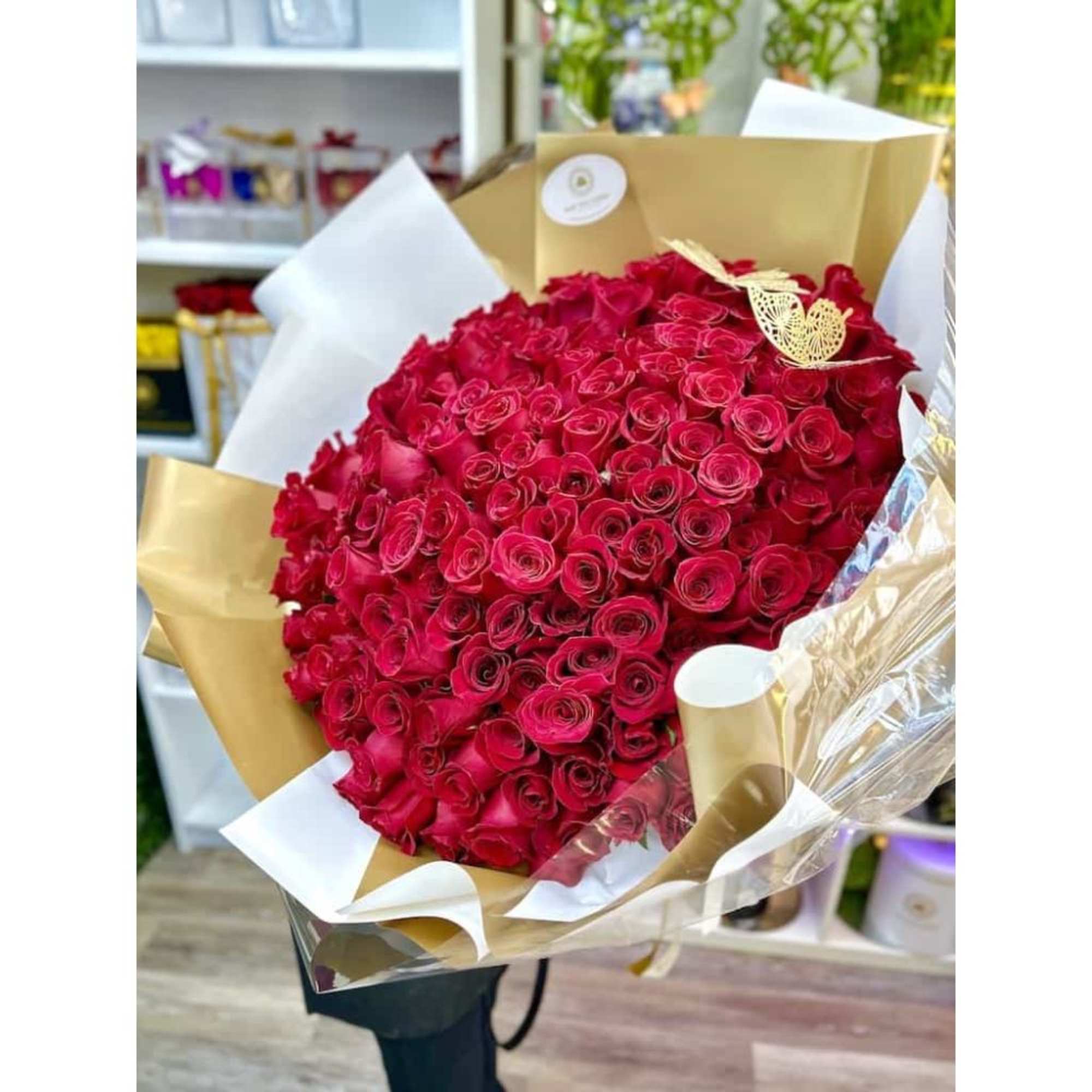 Large bouquet of tightly packed red roses wrapped in white and gold paper with a gold butterfly accent