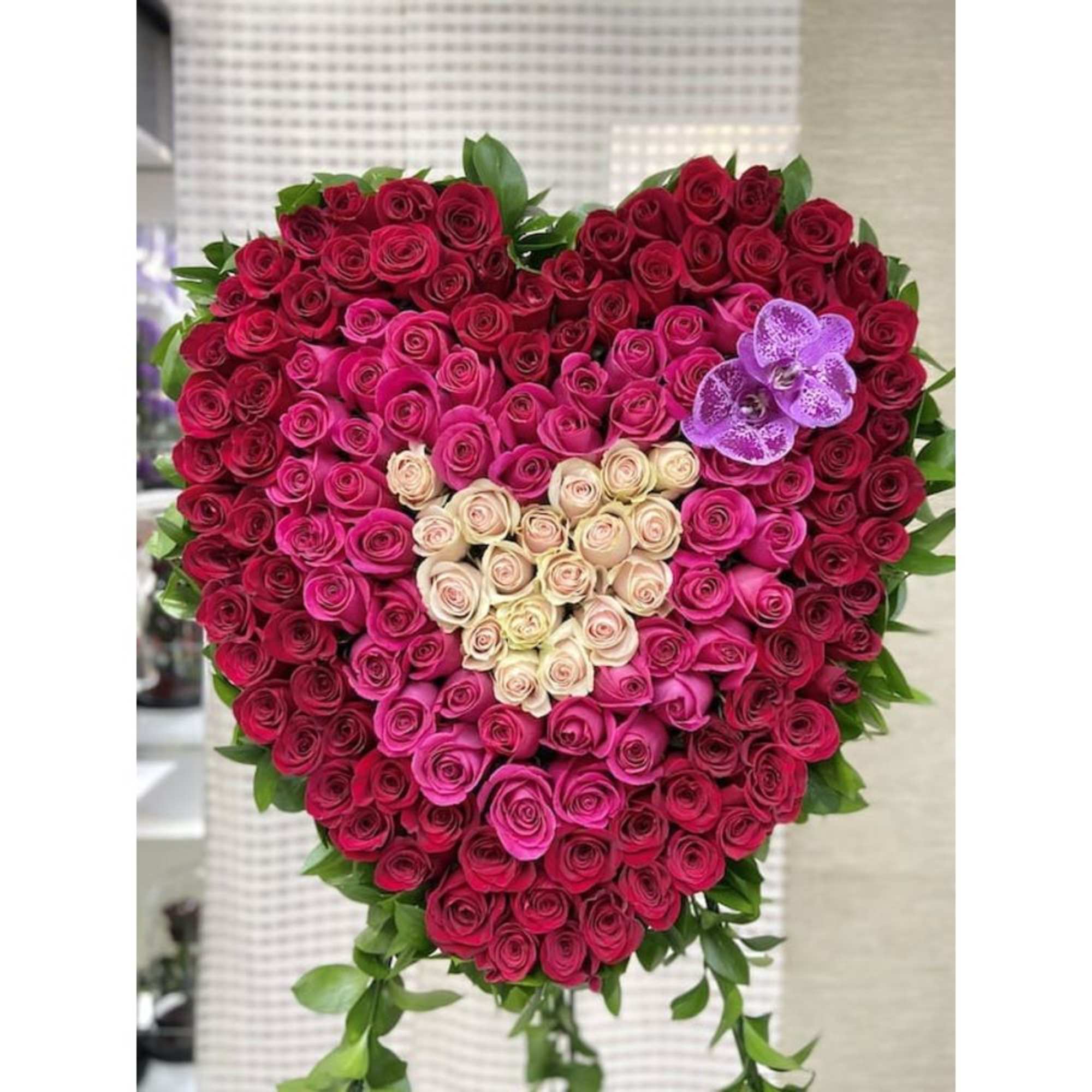 Heart-shaped arrangement of red, hot pink, and cream roses with a small inner heart and purple orchids.