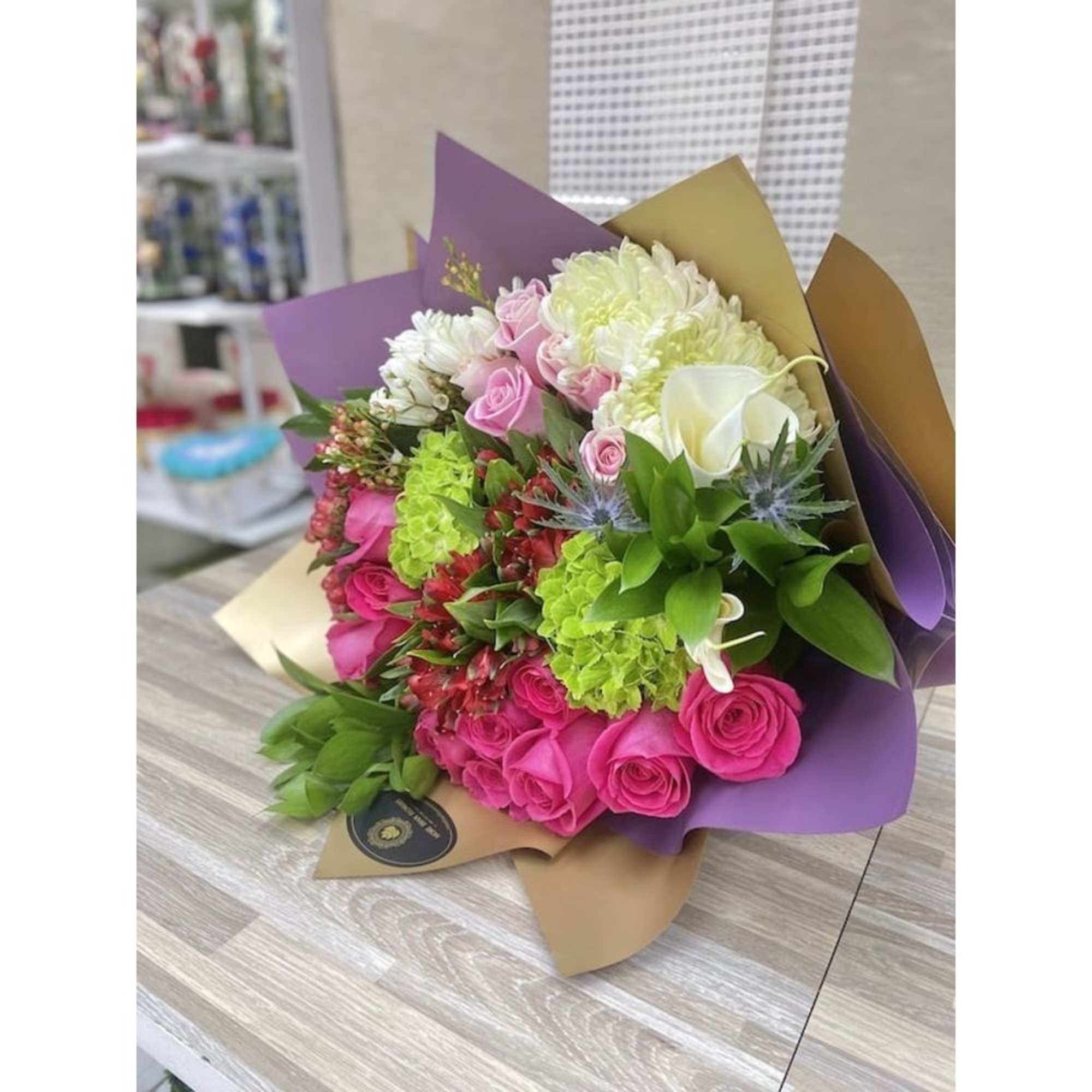 Hand-tied bouquet with hot pink roses, white blooms, and green accents wrapped in gold and purple paper