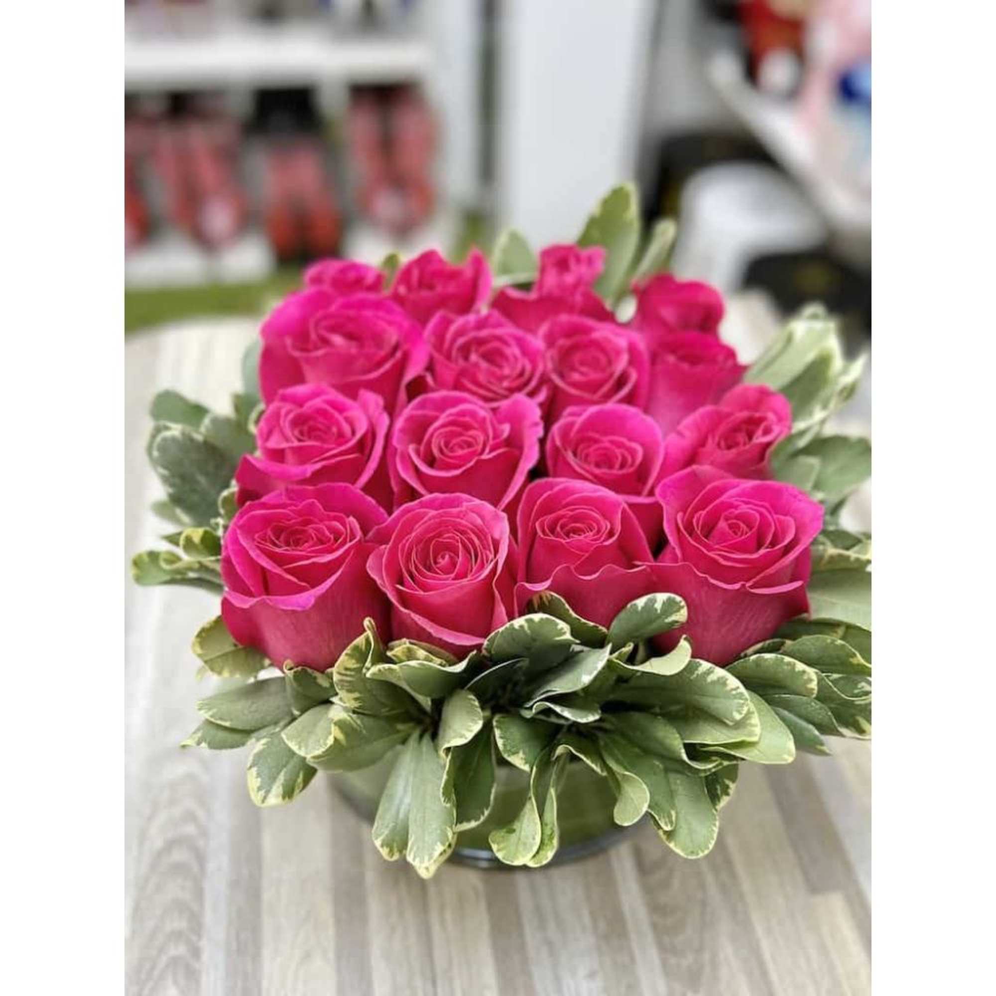 Low round arrangement of hot pink roses in a clear glass bowl with a ring of variegated foliage.