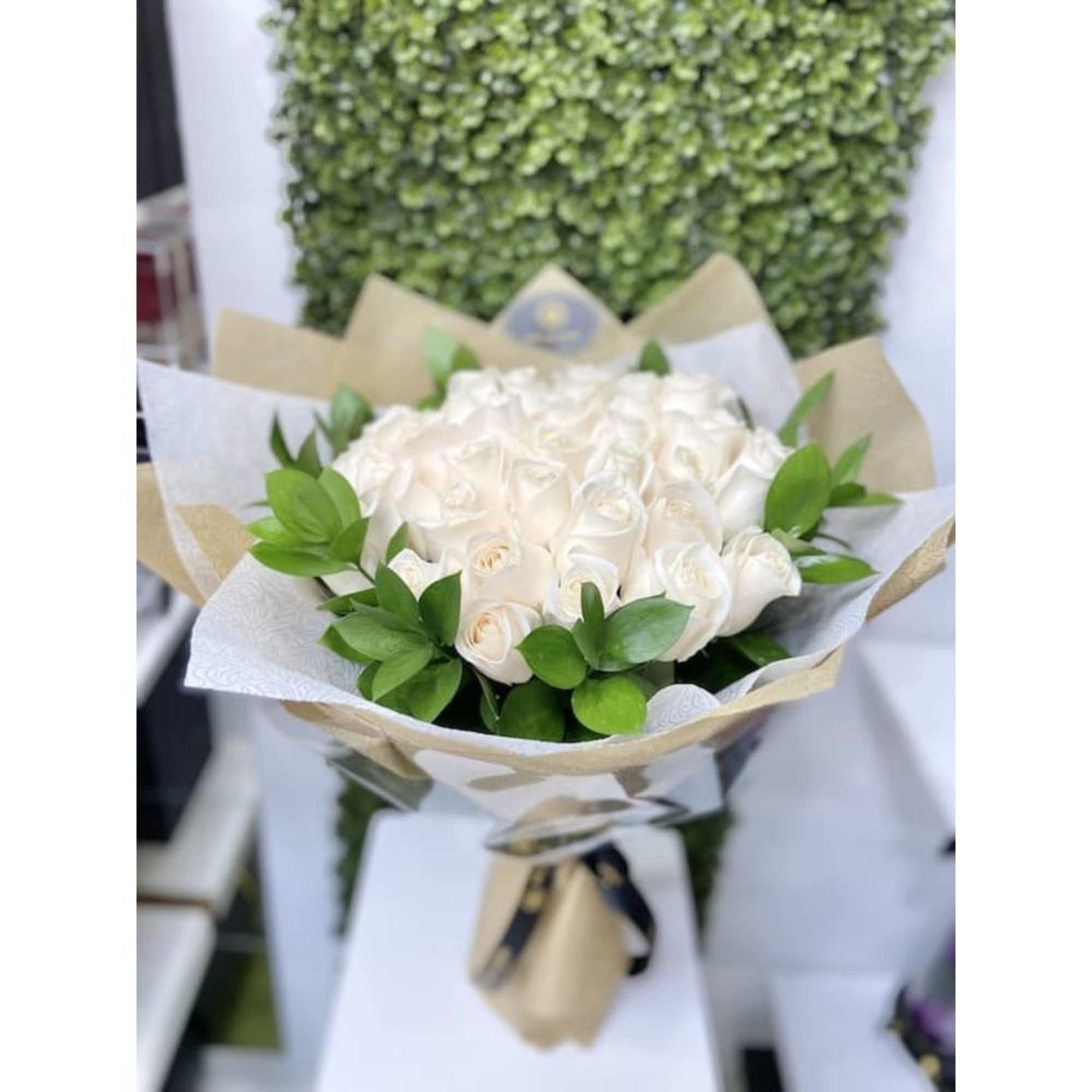 Hand-tied bouquet of white roses with green foliage accents wrapped in white and kraft paper