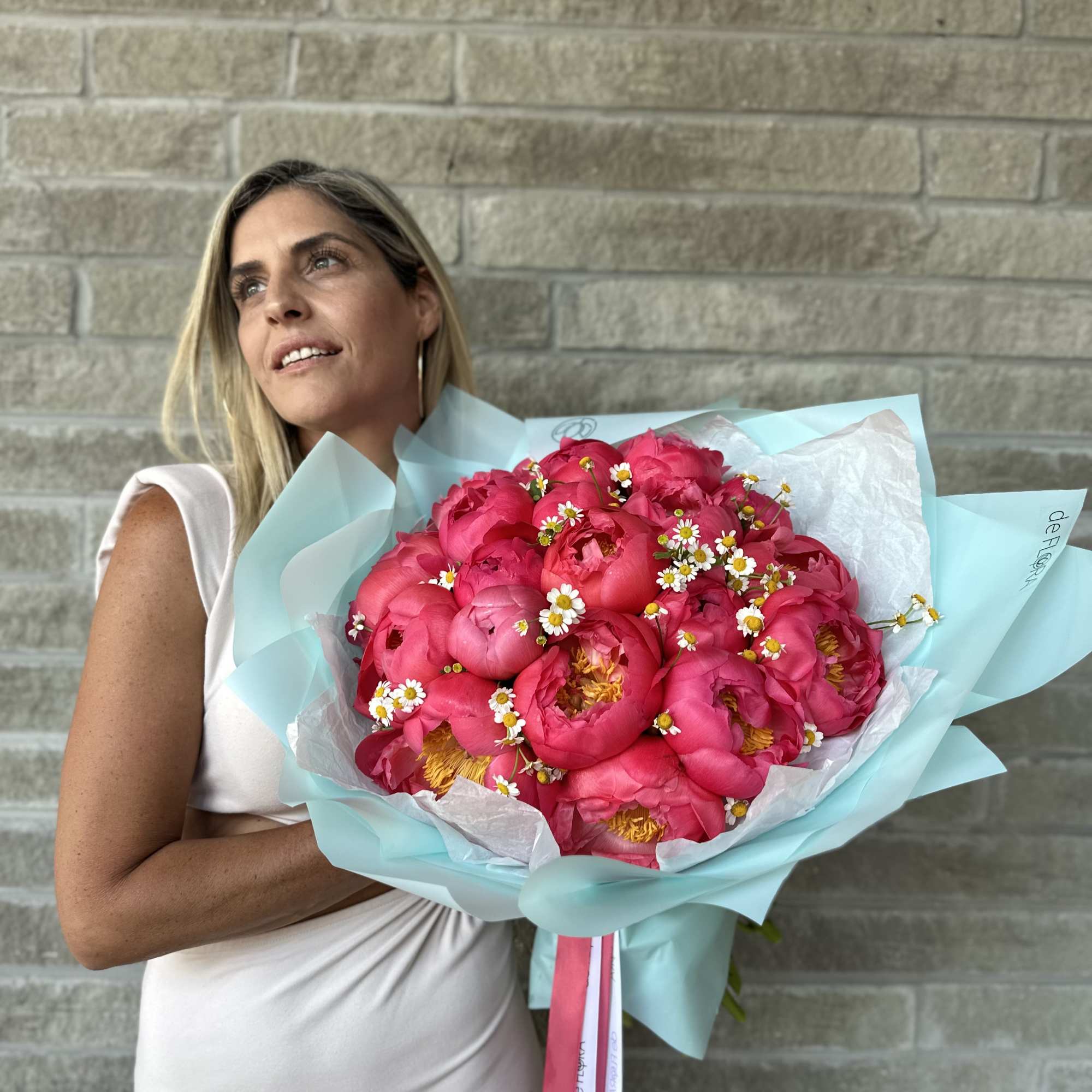 Woman holding a bouquet of bright pink peonies with small white daisies