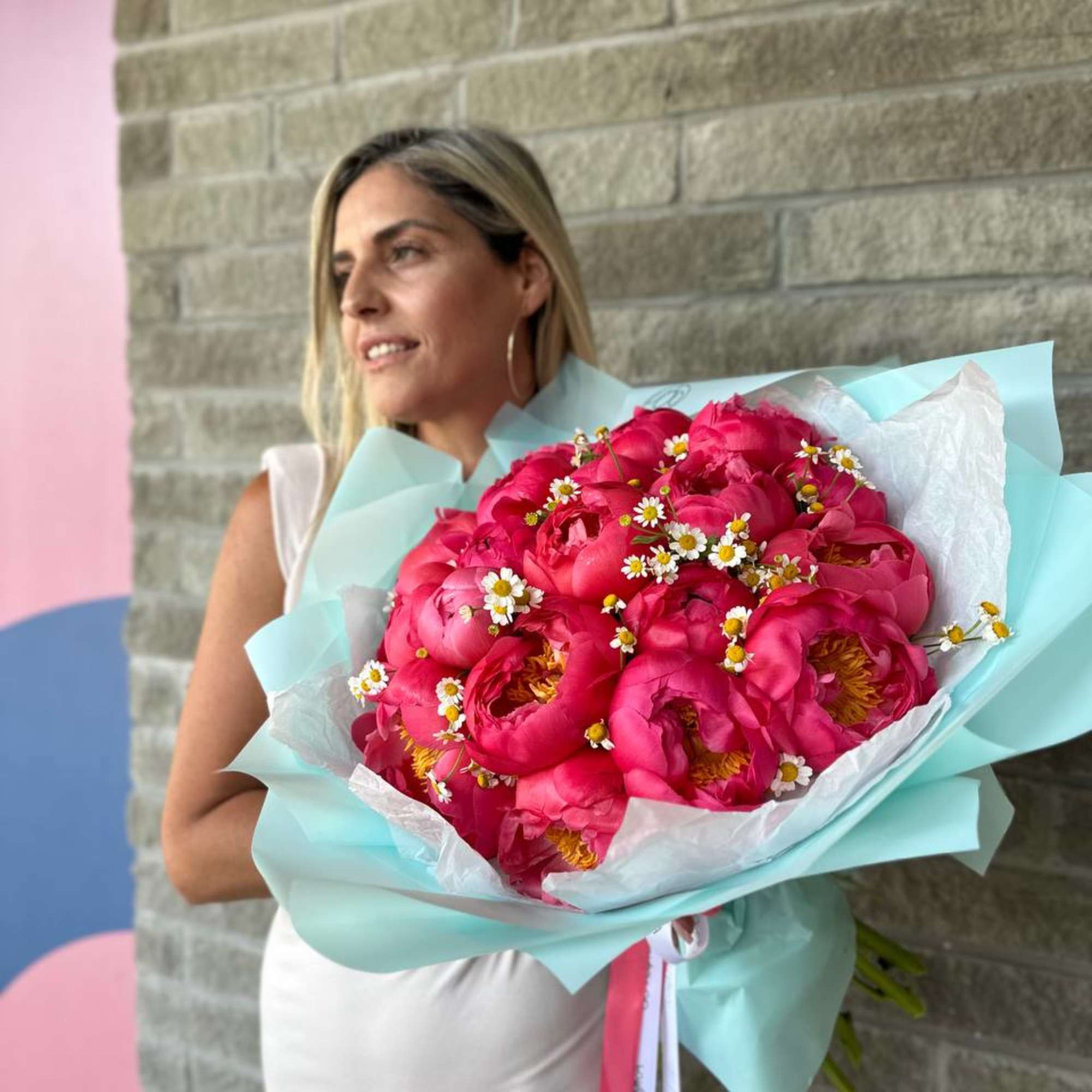 Woman holding a large bouquet of hot pink peonies with small white daisies
