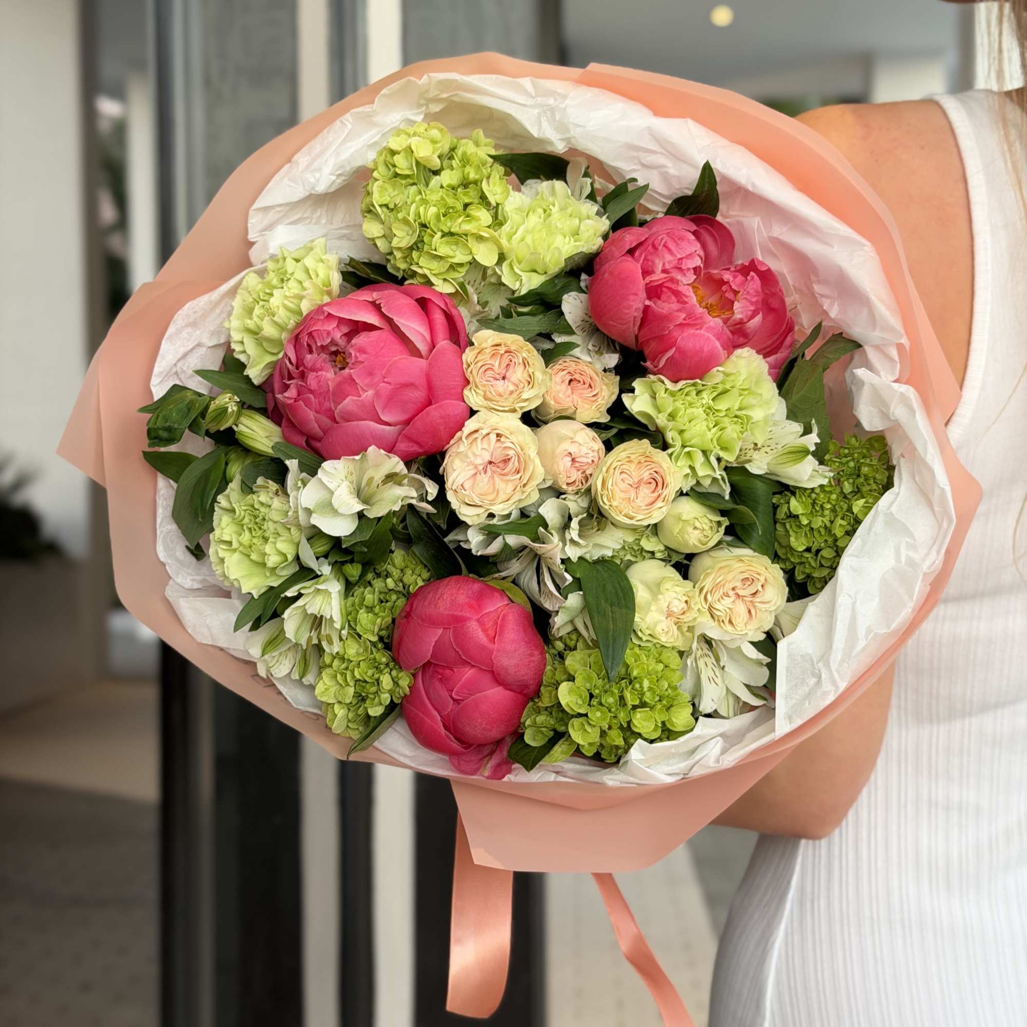Bouquet of pink peonies and green hydrangeas wrapped in peach paper