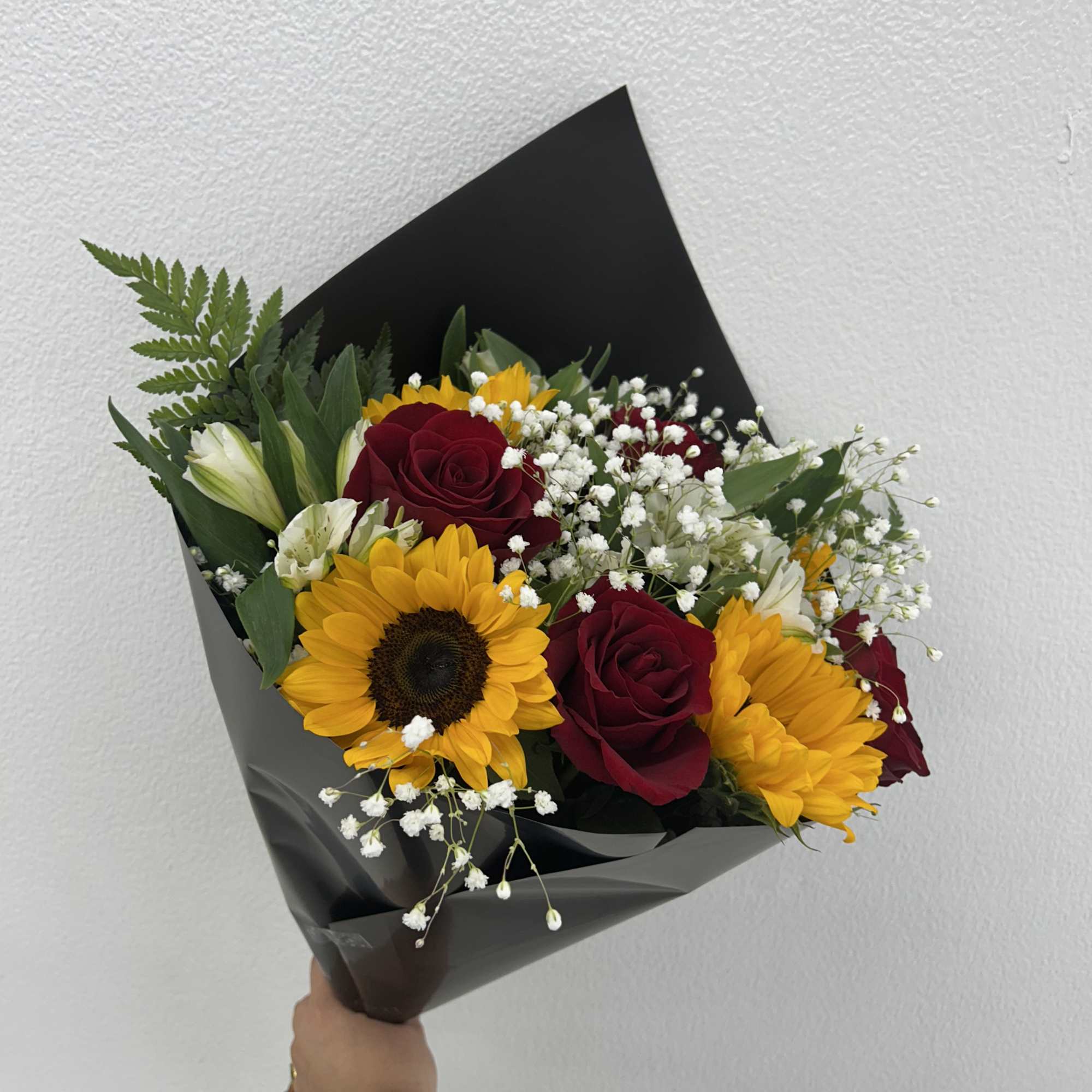 Bouquet of red roses, sunflowers, and white filler flowers in black wrap