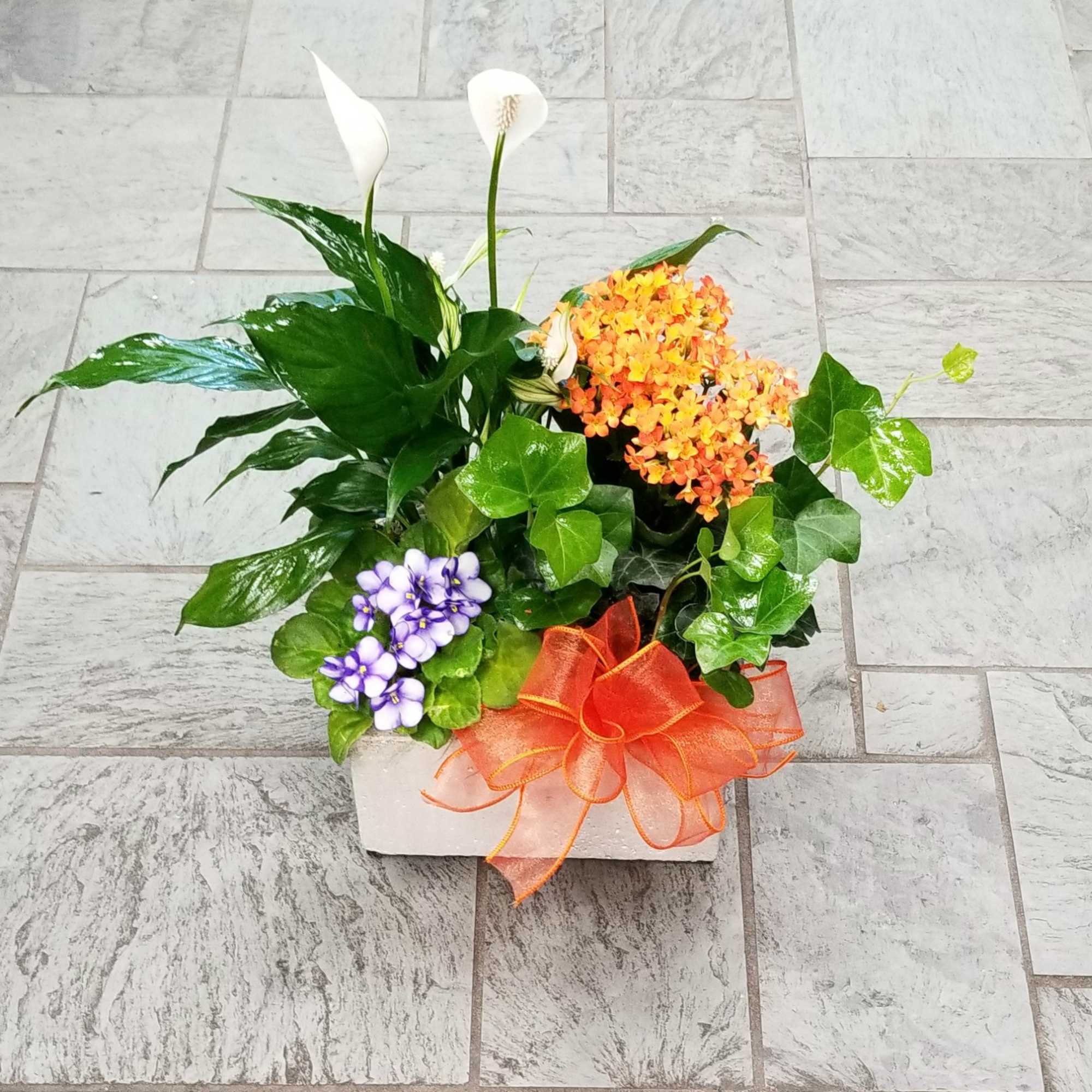 Potted arrangement with white calla lilies, orange flowers, and a purple cluster in a white container