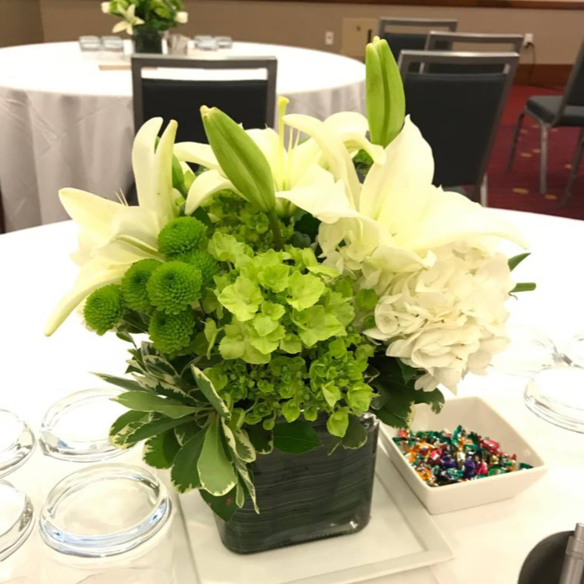 White lilies and green flowers arranged in a square vase